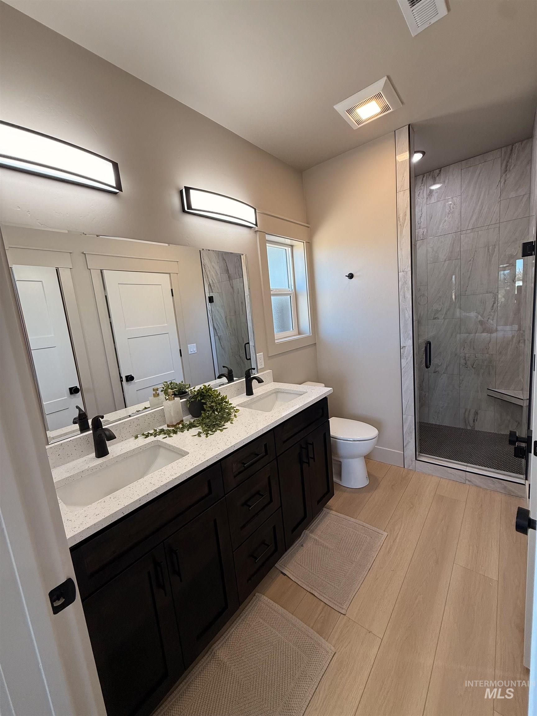 Full bath with a marble finish shower, double vanity, and light wood-type flooring