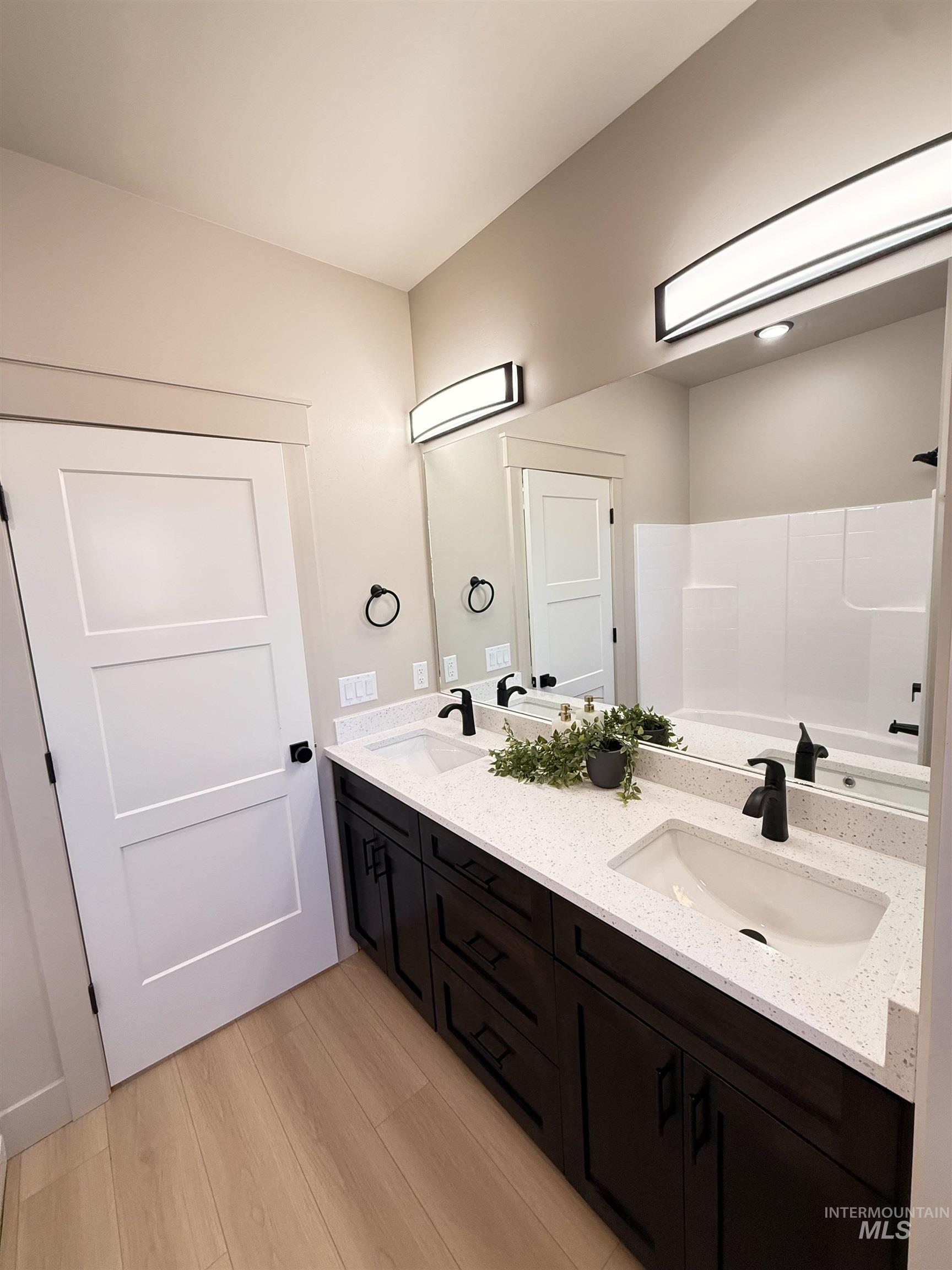 Full bathroom featuring double vanity, a bath, and light wood finished floors