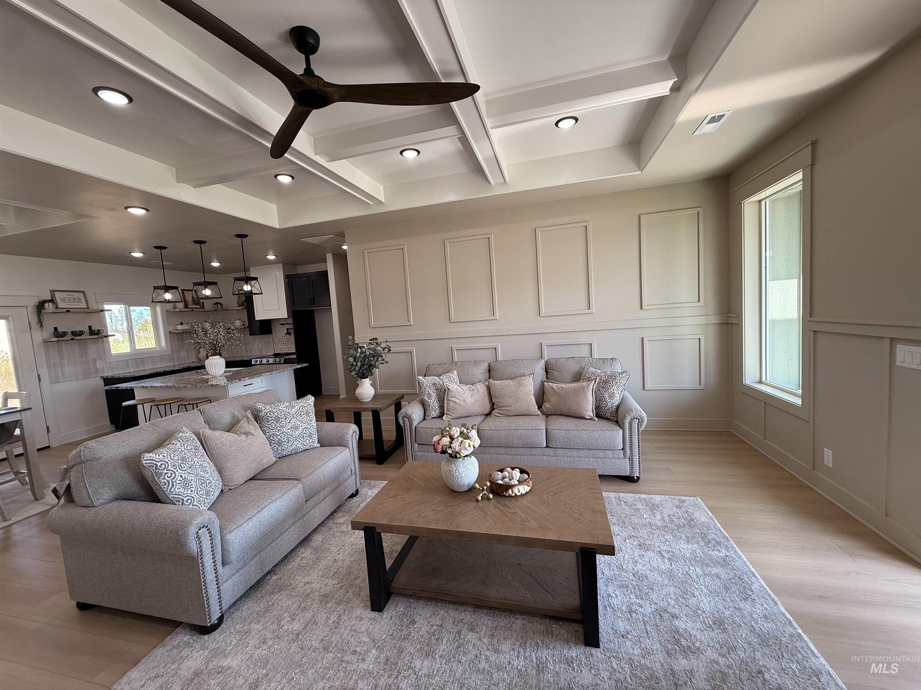 Living room featuring beamed ceiling, coffered ceiling, light wood-style flooring, a decorative wall, and ceiling fan