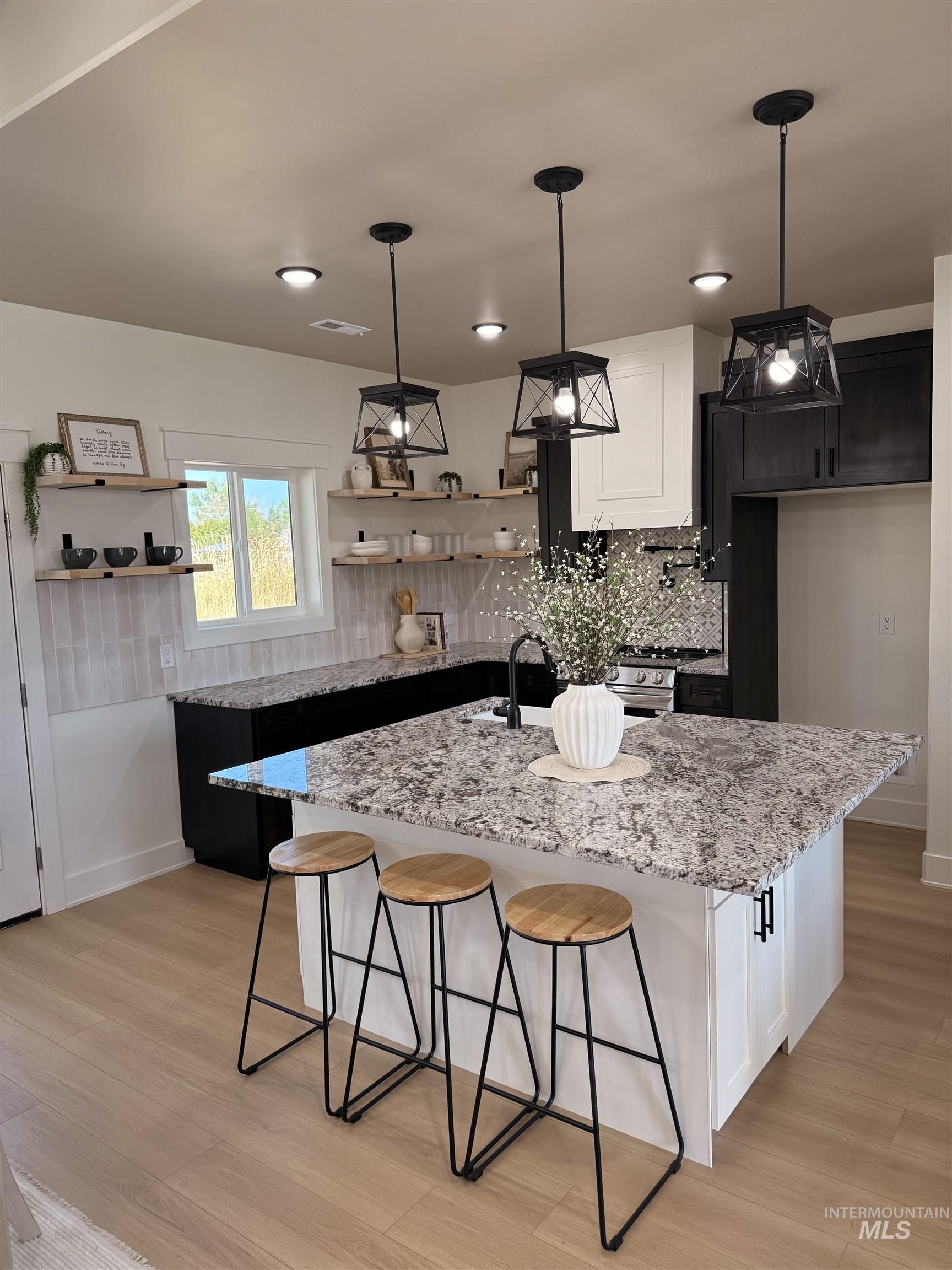Kitchen featuring backsplash, a kitchen bar, pendant lighting, a kitchen island with sink, and light stone countertops