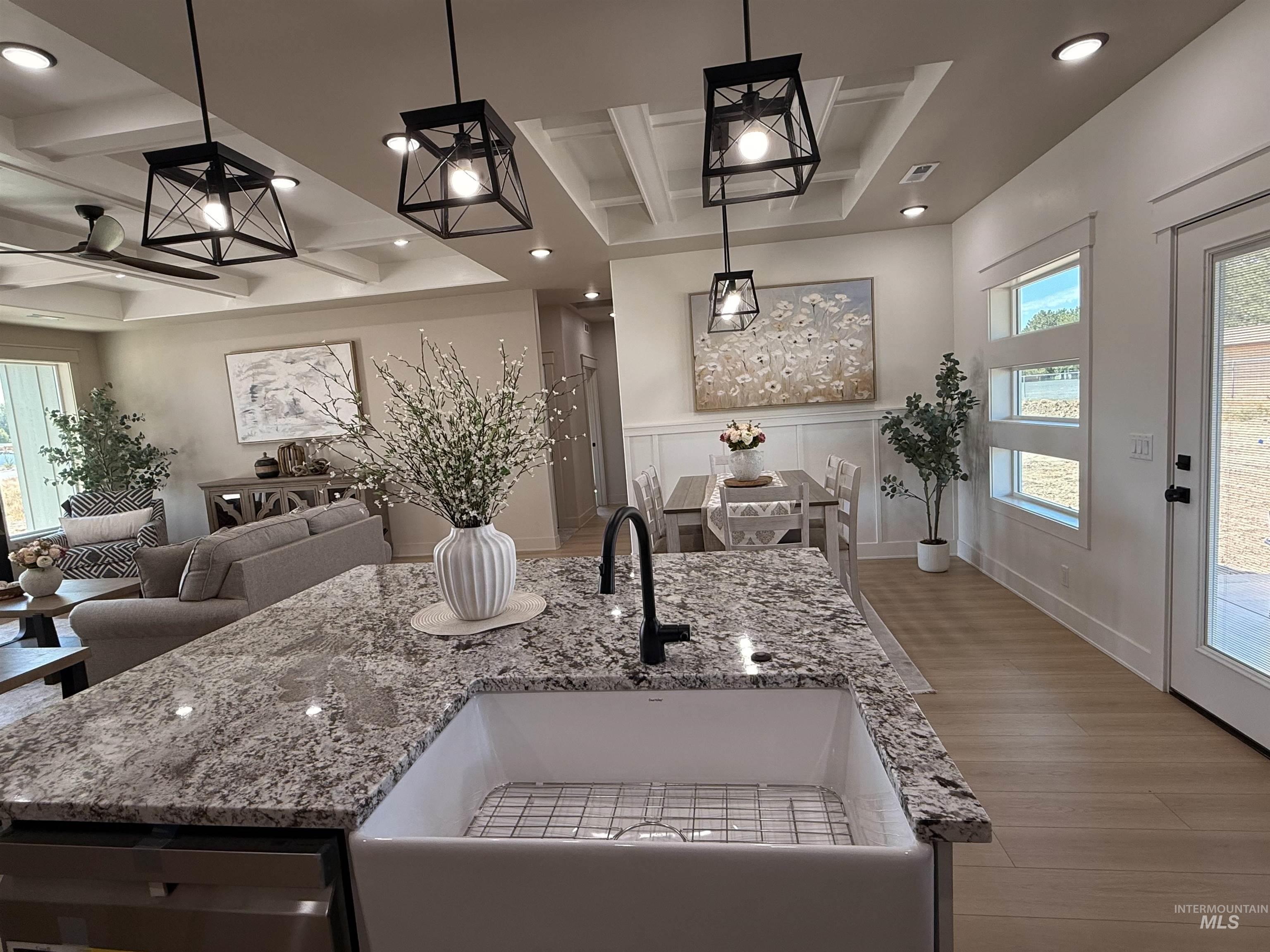 Kitchen featuring healthy amount of natural light, coffered ceiling, light stone countertops, a kitchen island with sink, and beamed ceiling