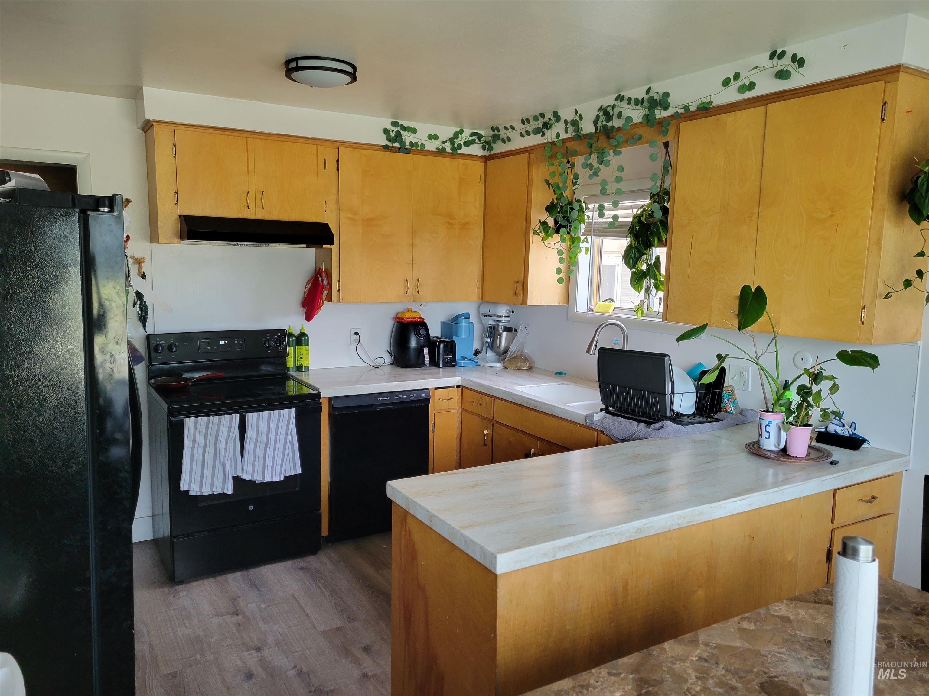 Kitchen featuring black appliances, a peninsula, light countertops, dark wood finished floors, and under cabinet range hood