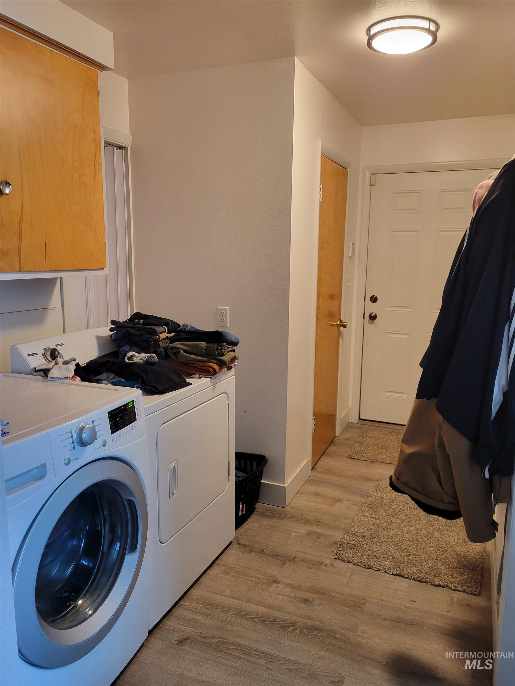 Laundry area featuring light wood-type flooring, independent washer and dryer, and cabinet space