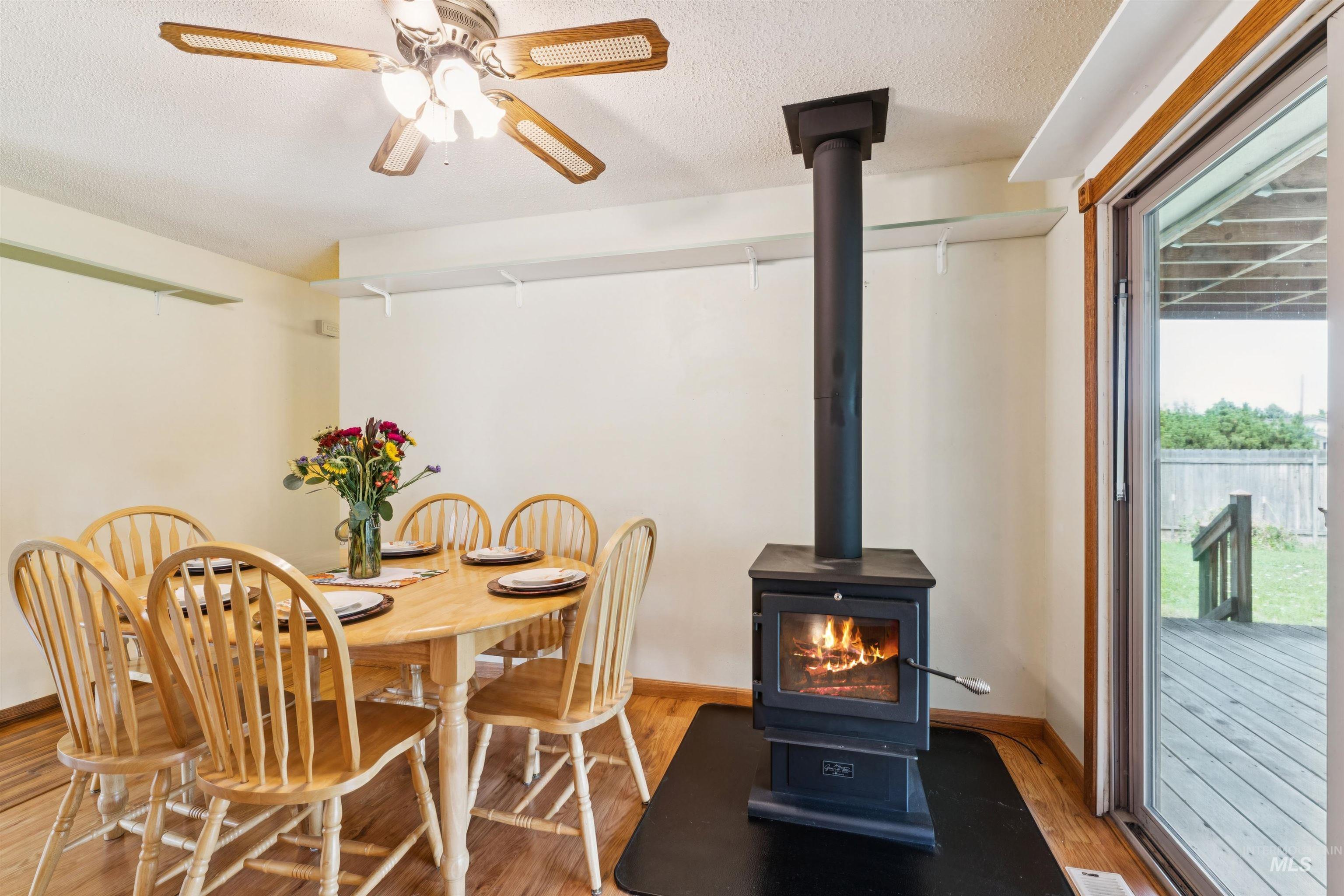 Dining area with a wood stove, light wood-style flooring, a textured ceiling, and ceiling fan