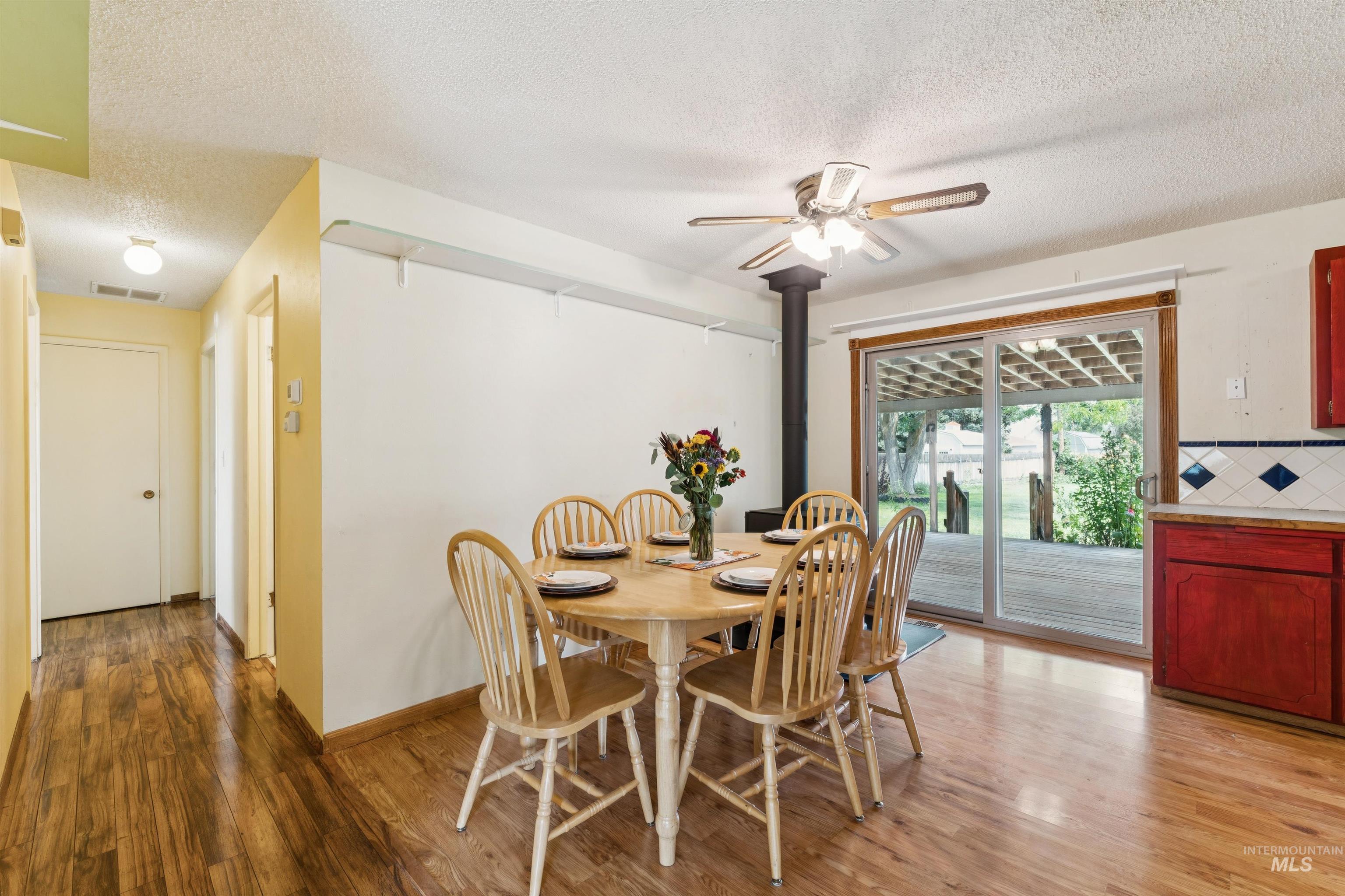 Dining room featuring light wood-style flooring, a textured ceiling, a wood stove, and ceiling fan