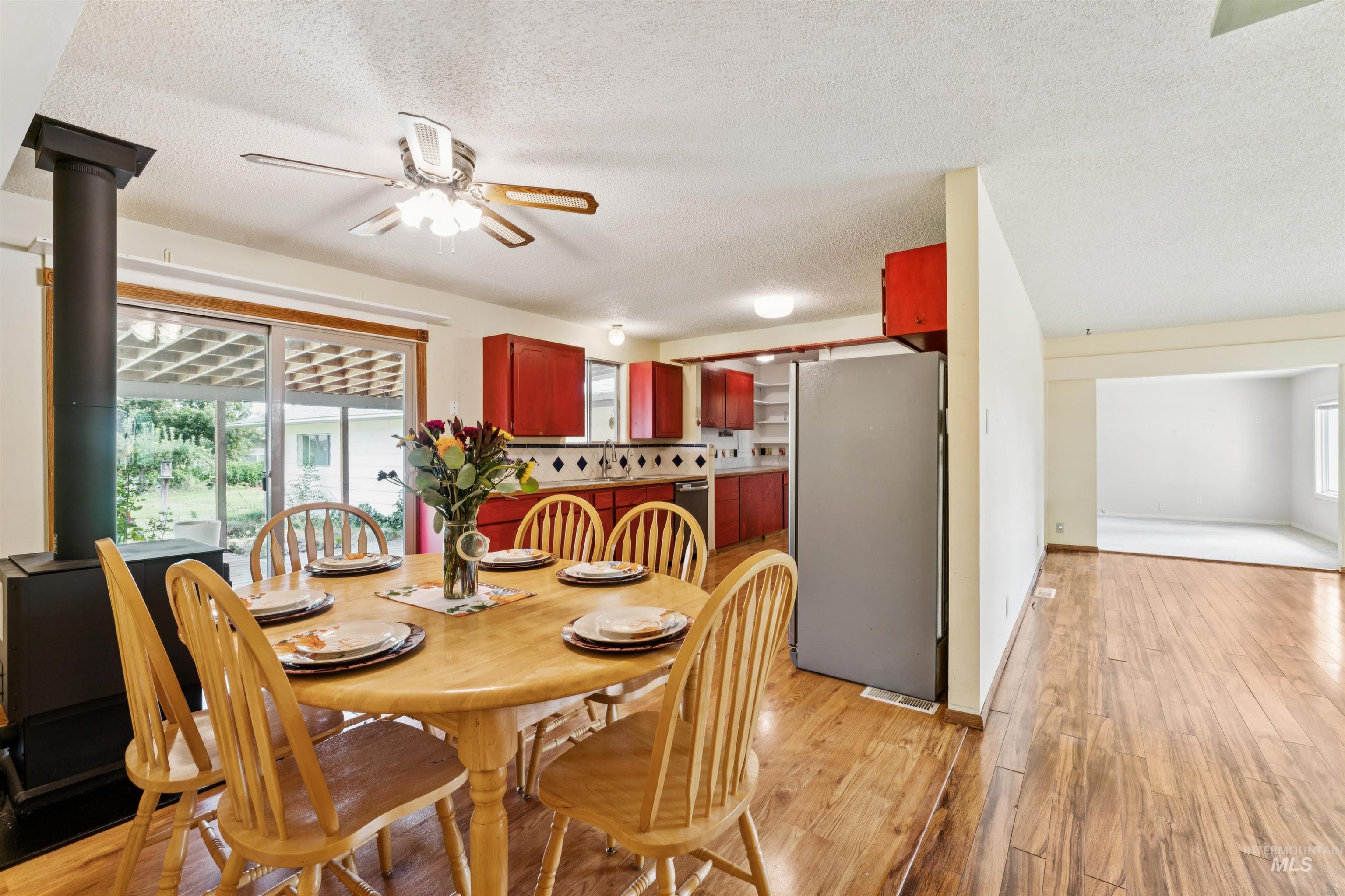 Dining area with light wood-style floors, a textured ceiling, a wood stove, and ceiling fan