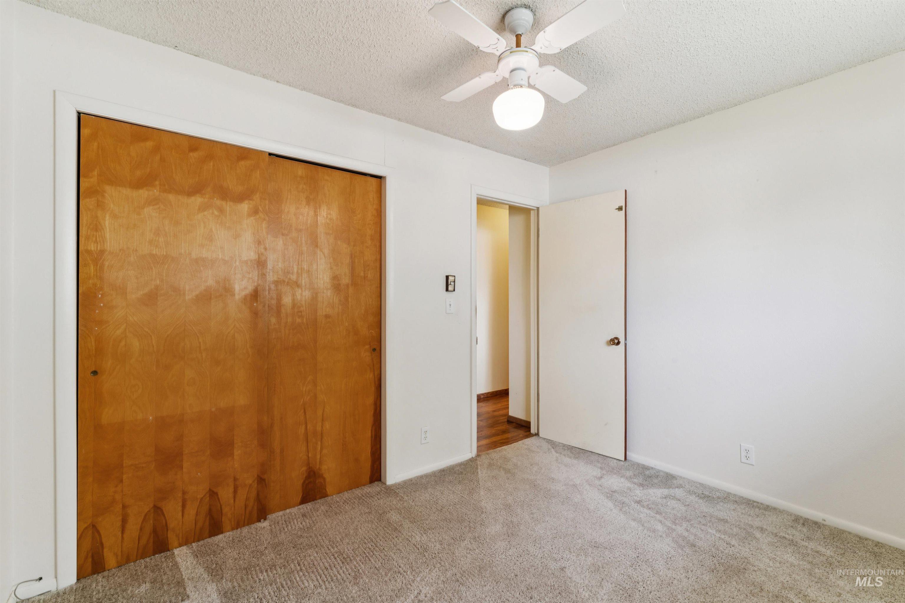 Unfurnished bedroom featuring a textured ceiling, a closet, carpet flooring, and a ceiling fan