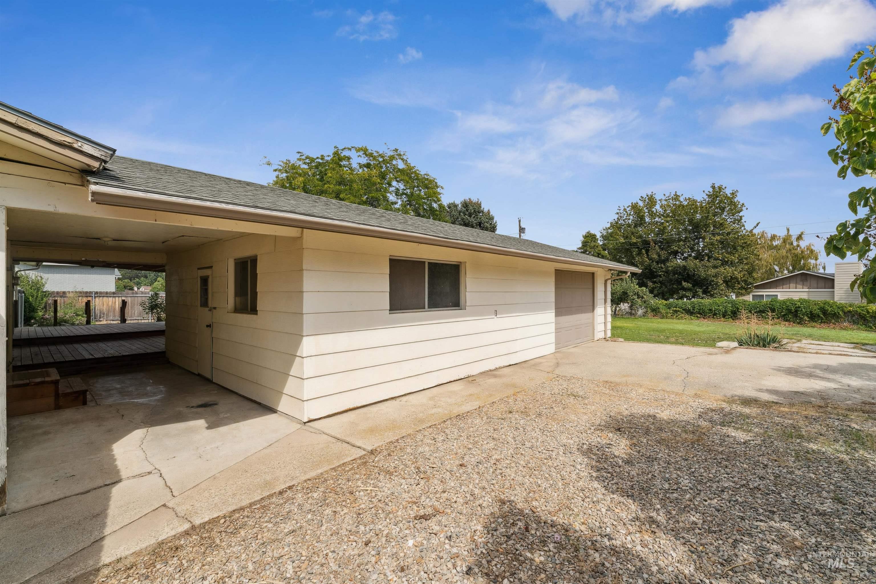 View of side of property with a shingled roof, concrete driveway, a garage, and a patio area