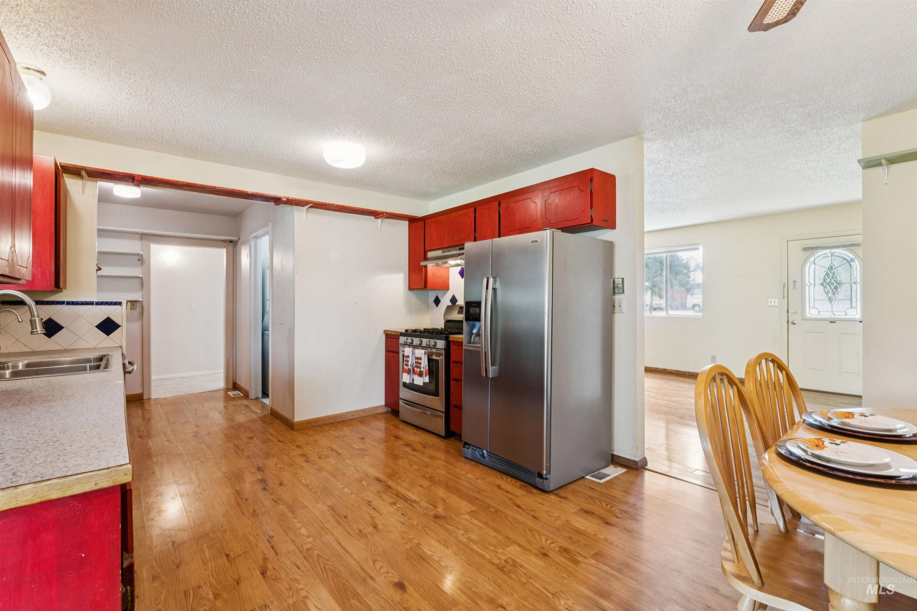 Kitchen with appliances with stainless steel finishes, light countertops, light wood-style flooring, a textured ceiling, and decorative backsplash