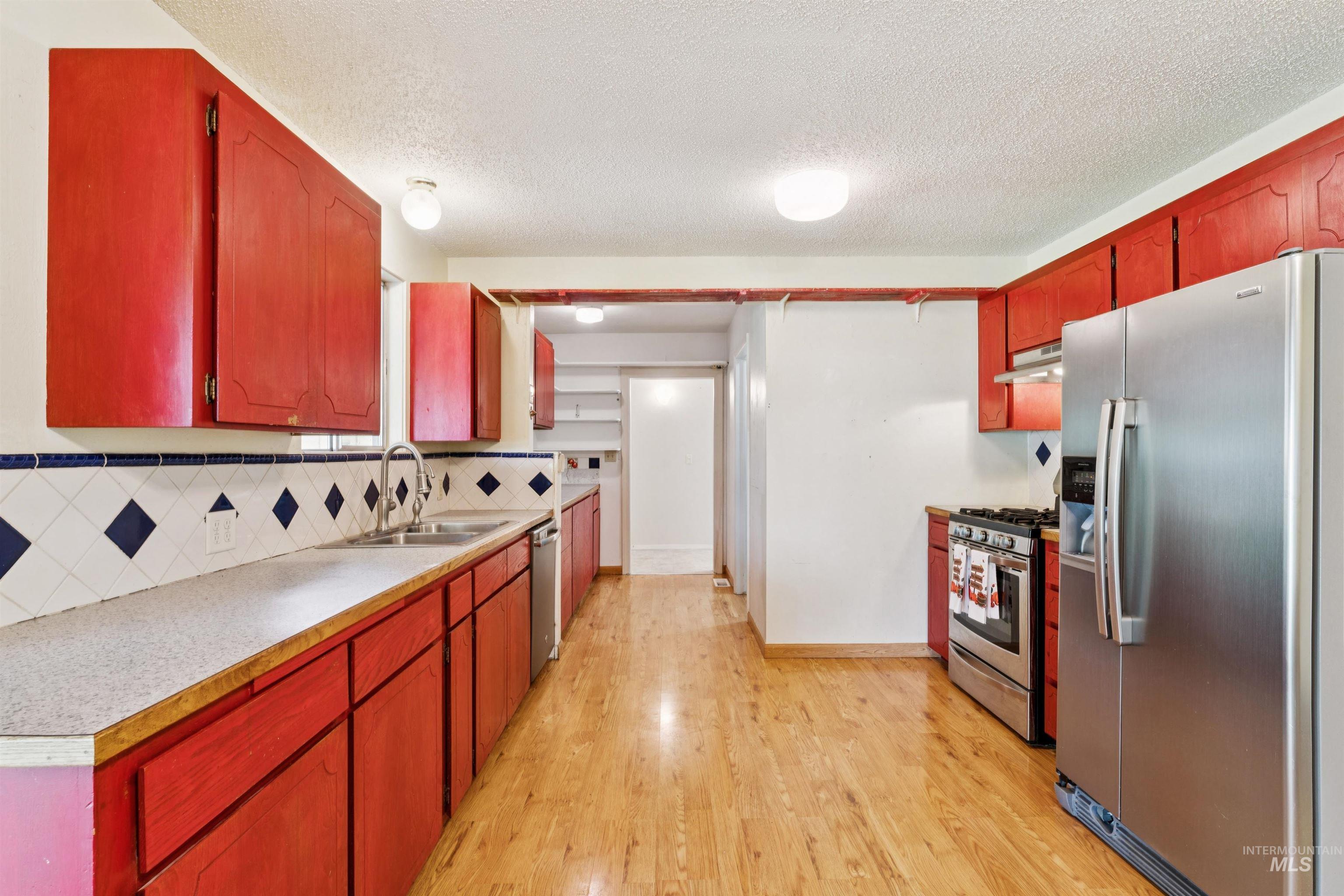 Kitchen featuring stainless steel appliances, light countertops, light wood-style flooring, decorative backsplash, and a textured ceiling