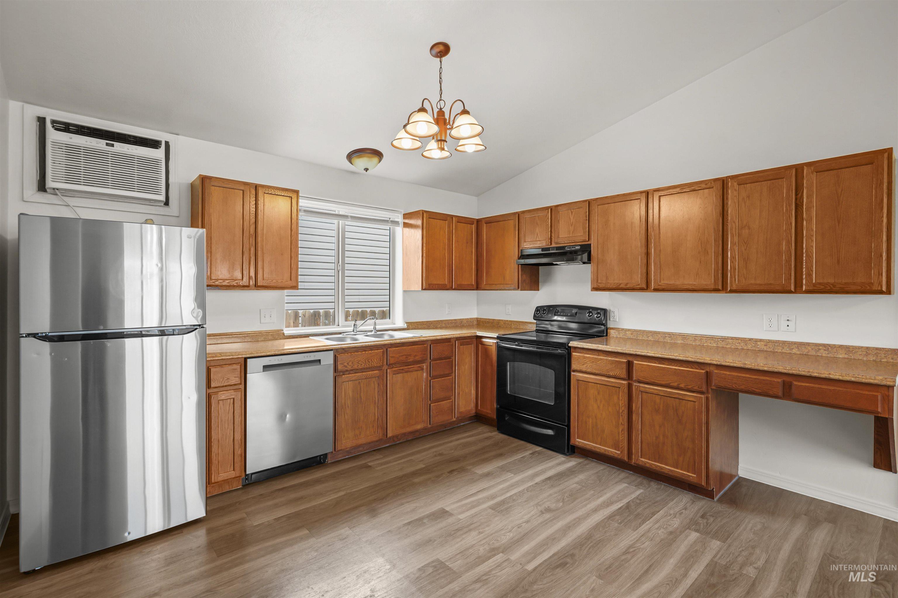 Kitchen featuring stainless steel appliances, light countertops, vaulted ceiling, dark wood-type flooring, and brown cabinetry