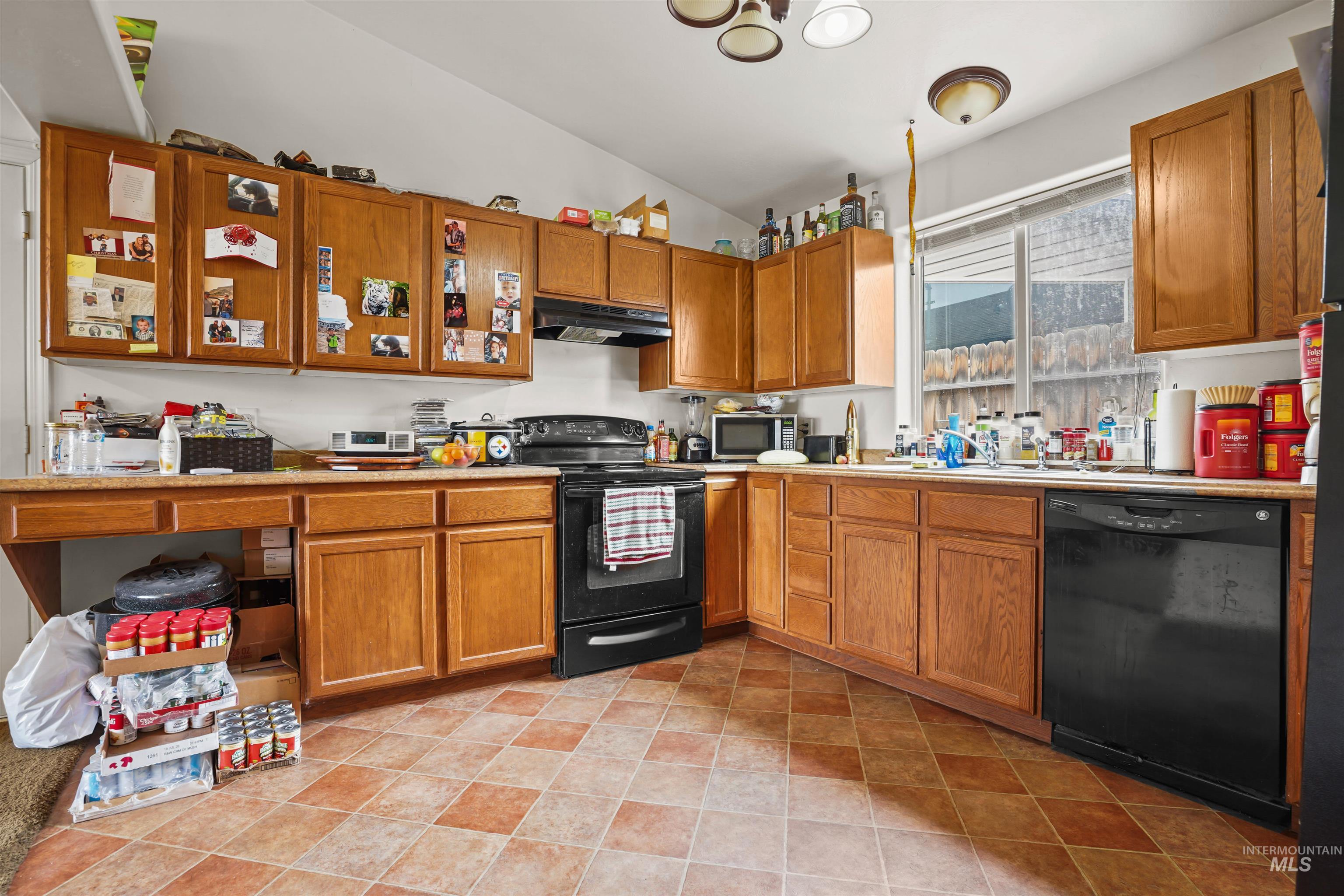 Kitchen featuring black appliances, light countertops, brown cabinets, vaulted ceiling, and under cabinet range hood