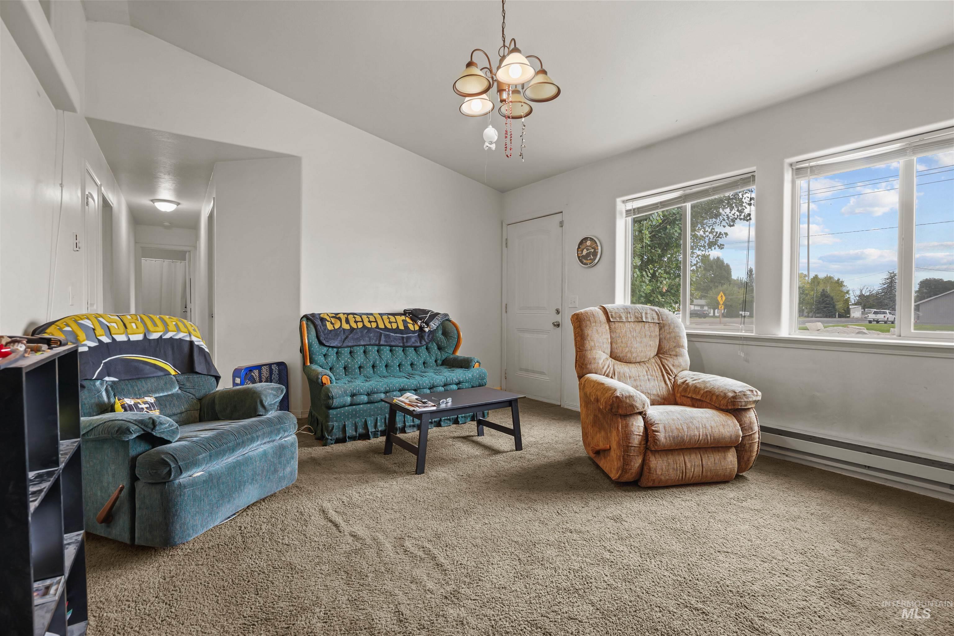 Sitting room with carpet flooring, a chandelier, a baseboard heating unit, and vaulted ceiling