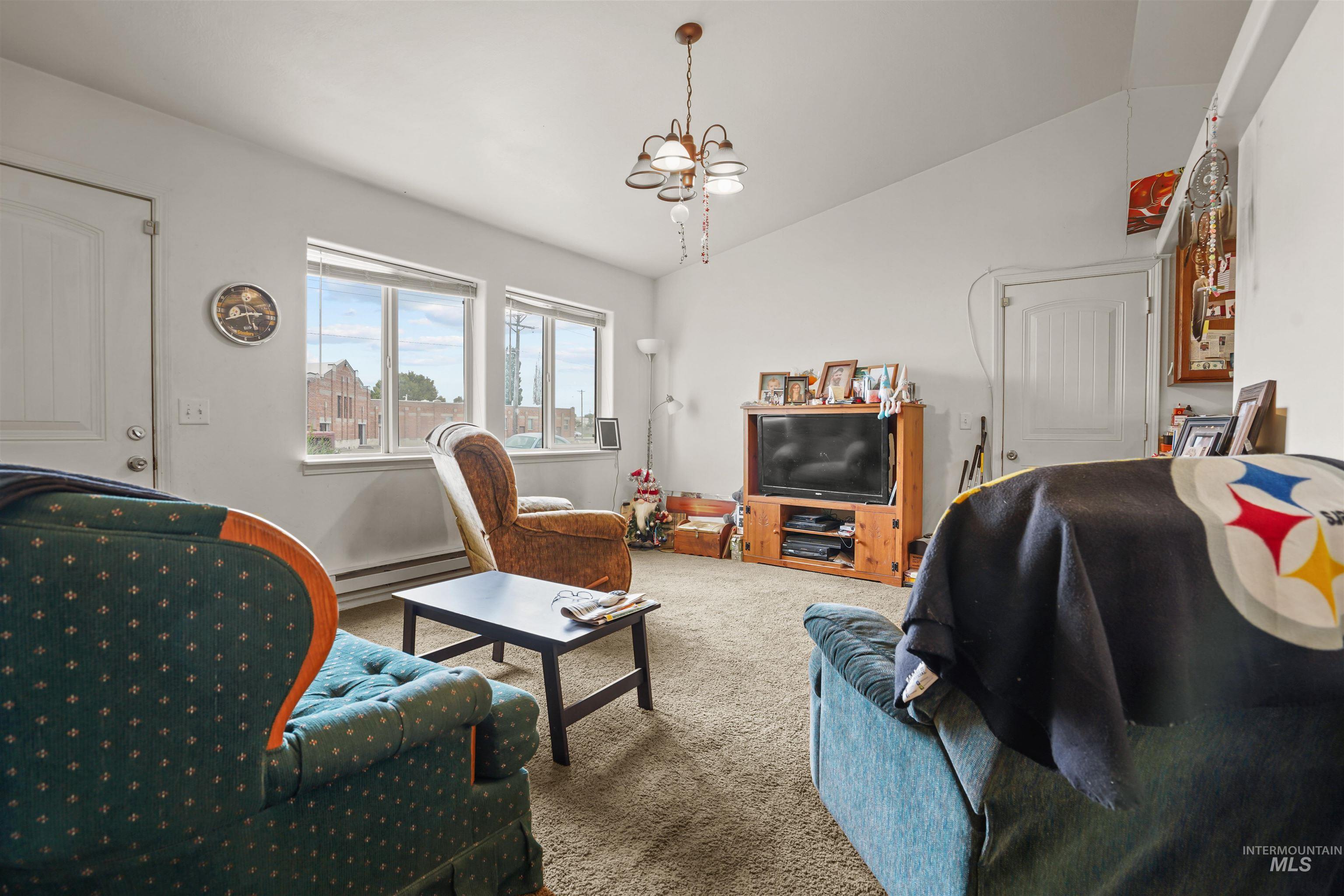Carpeted living room featuring lofted ceiling, a baseboard radiator, and a chandelier
