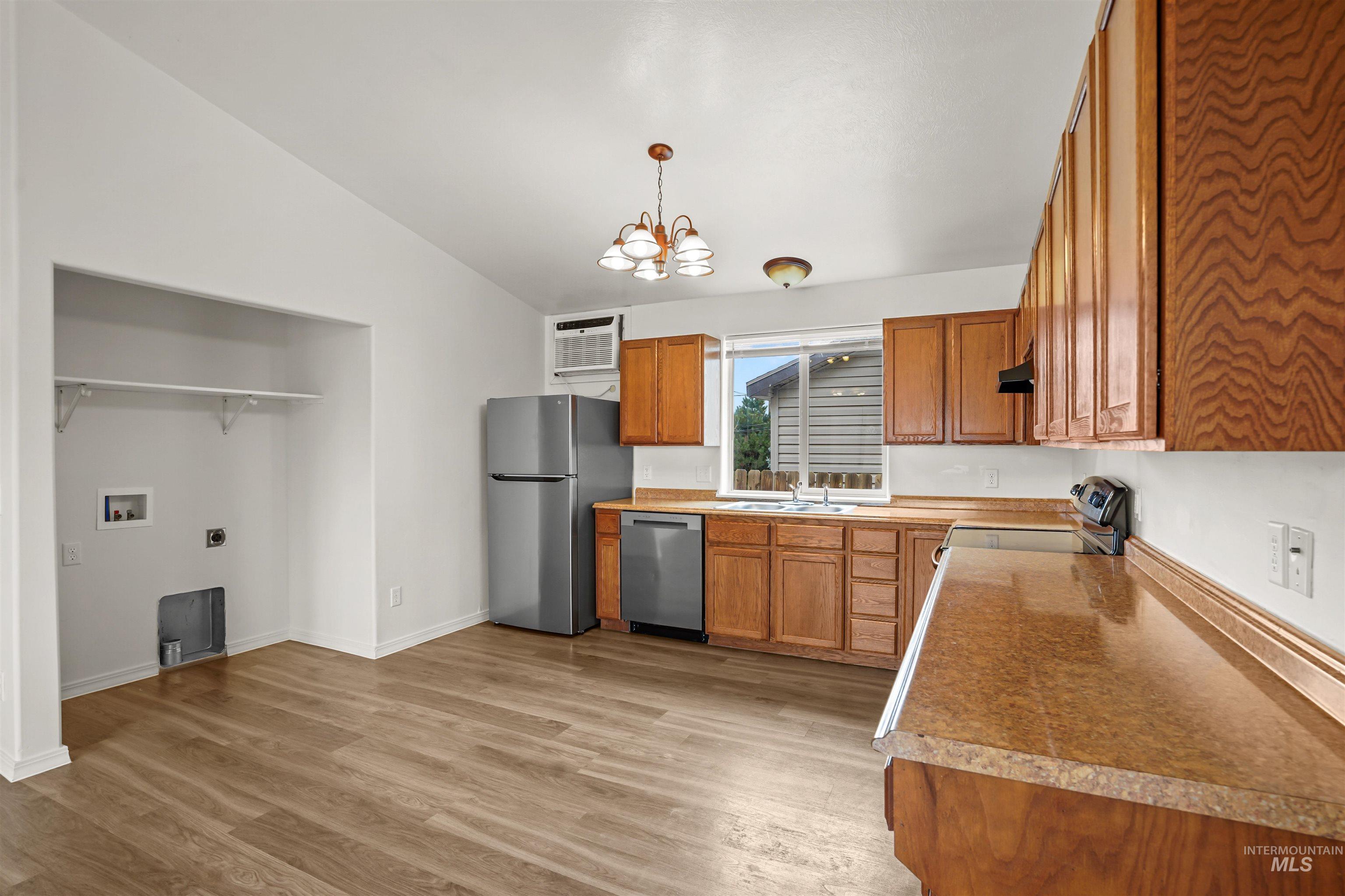 Kitchen featuring brown cabinets, light wood-style floors, a chandelier, appliances with stainless steel finishes, and decorative light fixtures
