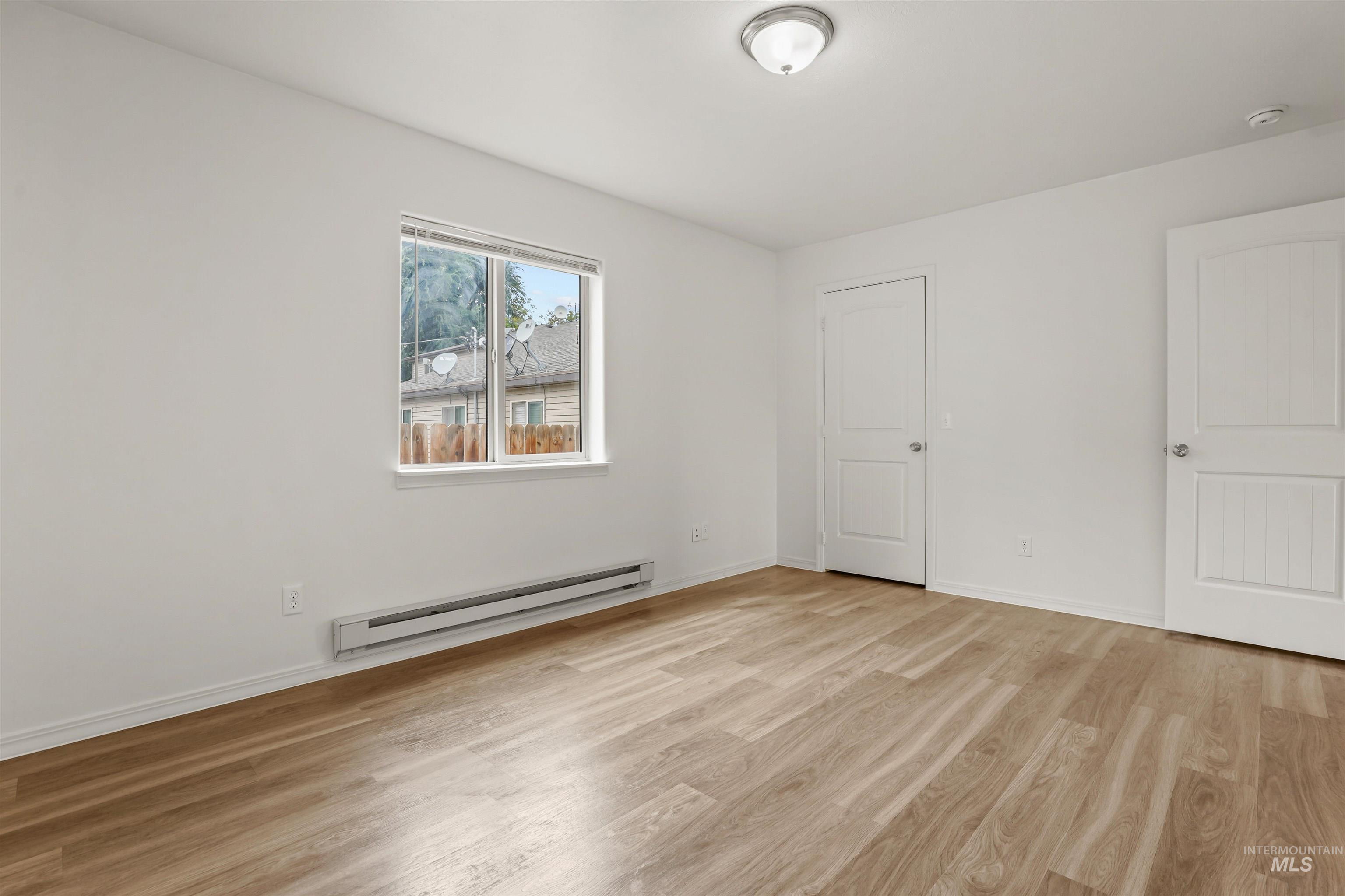 Unfurnished bedroom featuring a baseboard heating unit and light wood finished floors