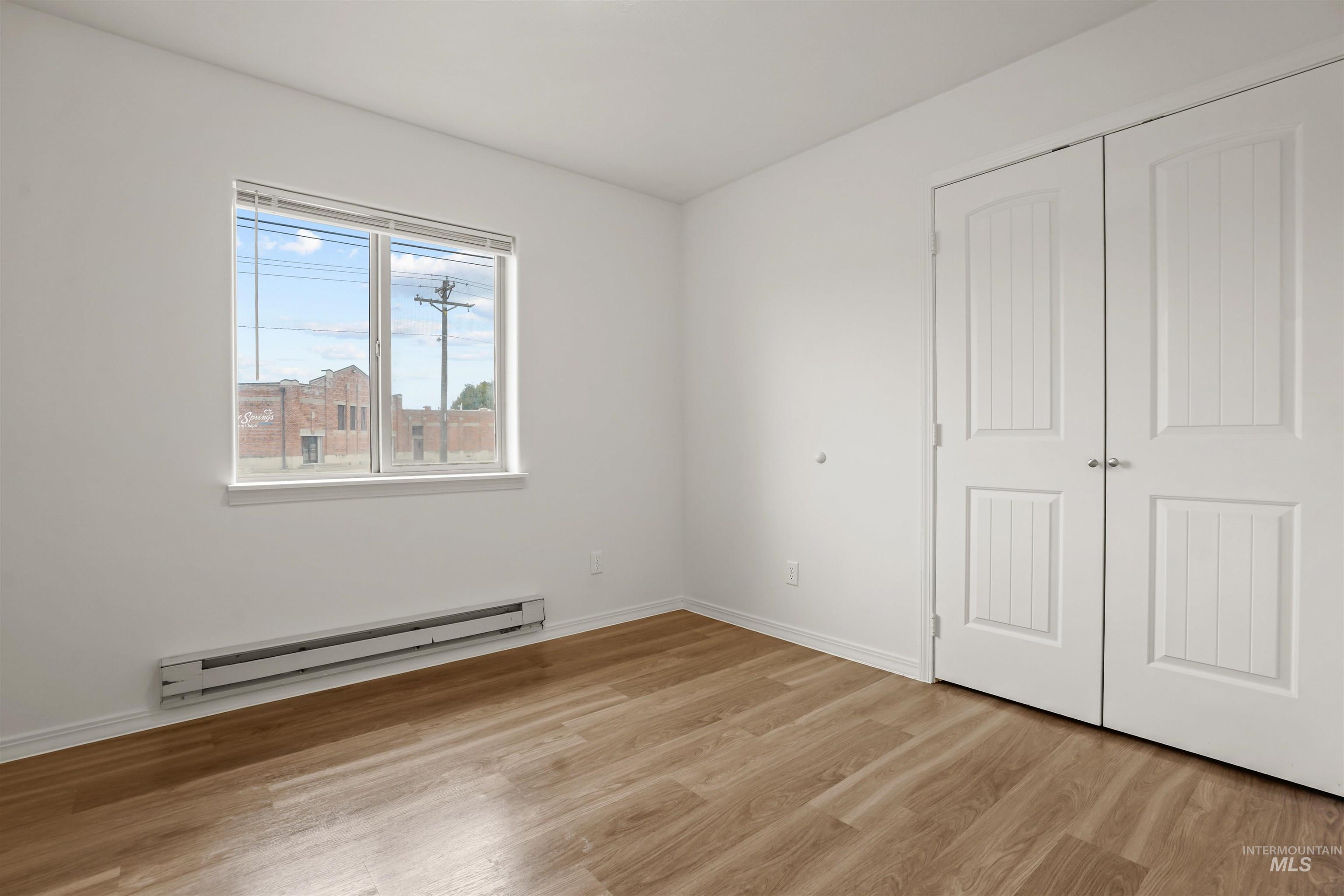 Unfurnished bedroom with baseboard heating, light wood-style floors, and a closet