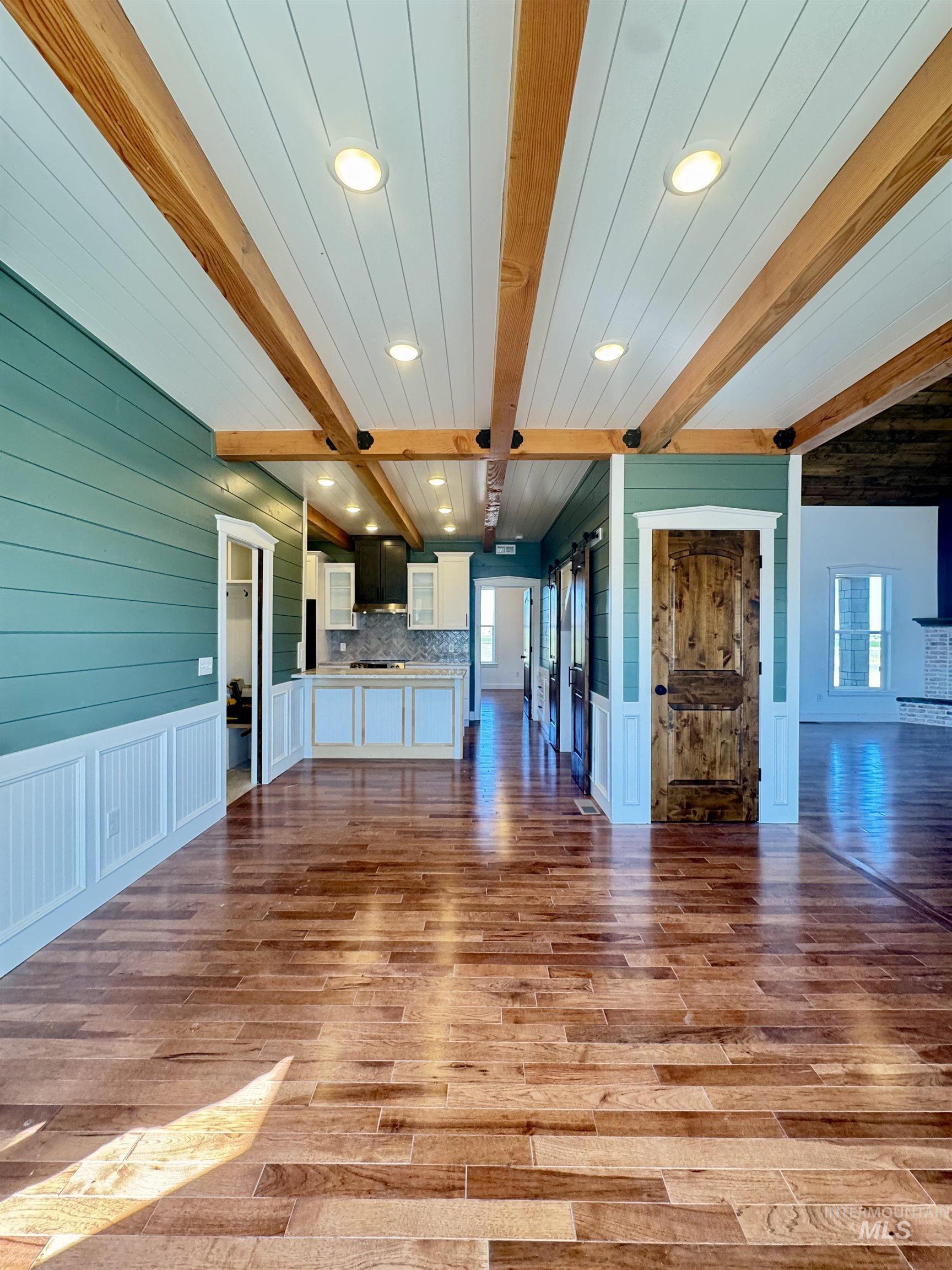 Unfurnished living room with beamed ceiling, light wood finished floors, recessed lighting, a decorative wall, and a wainscoted wall