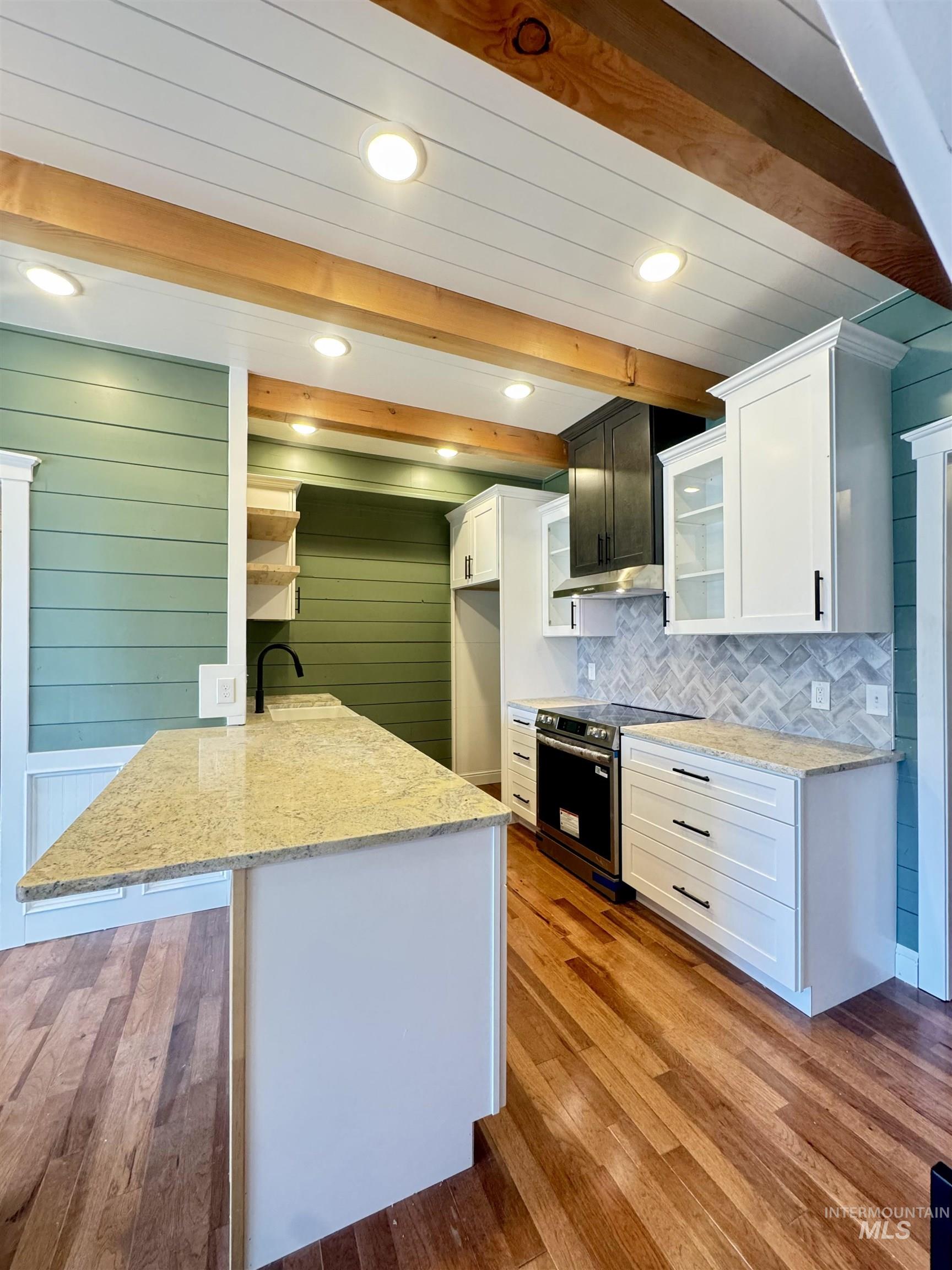 Kitchen with light stone counters, a peninsula, white cabinets, tasteful backsplash, and beam ceiling