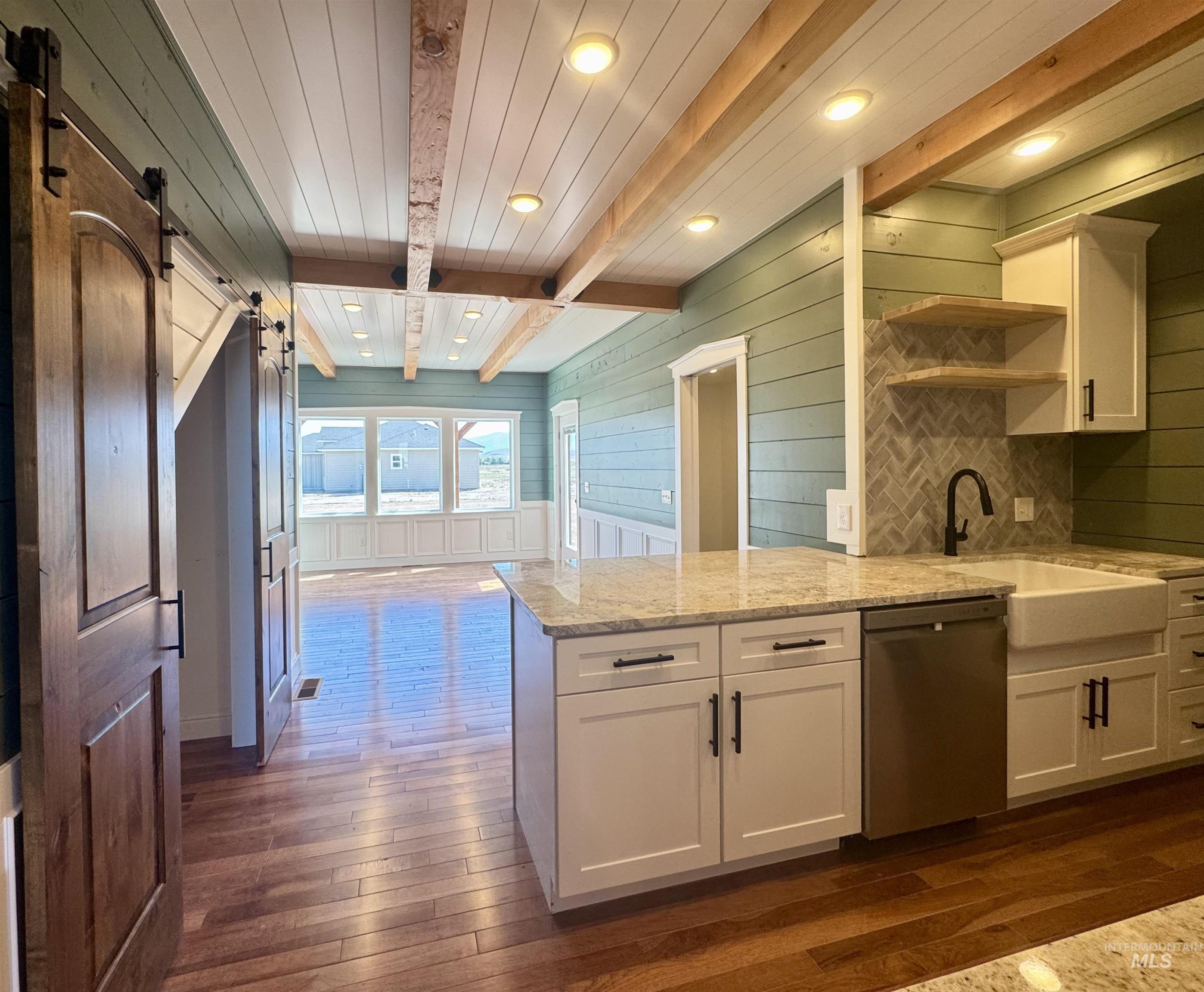 Kitchen featuring light stone counters, beam ceiling, white cabinetry, dishwasher, and a peninsula