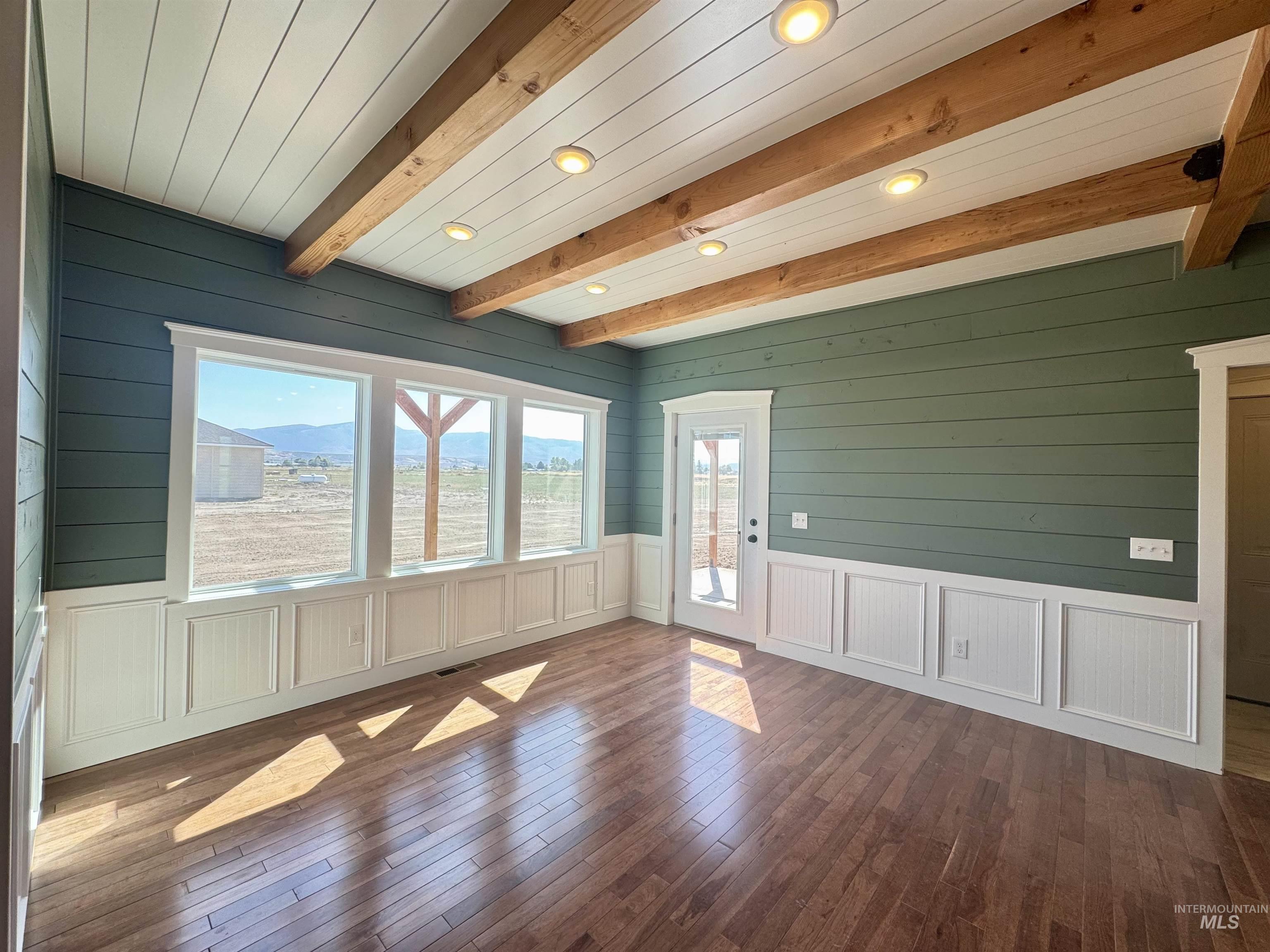 Empty room with beam ceiling, dark wood finished floors, recessed lighting, wood walls, and a decorative wall