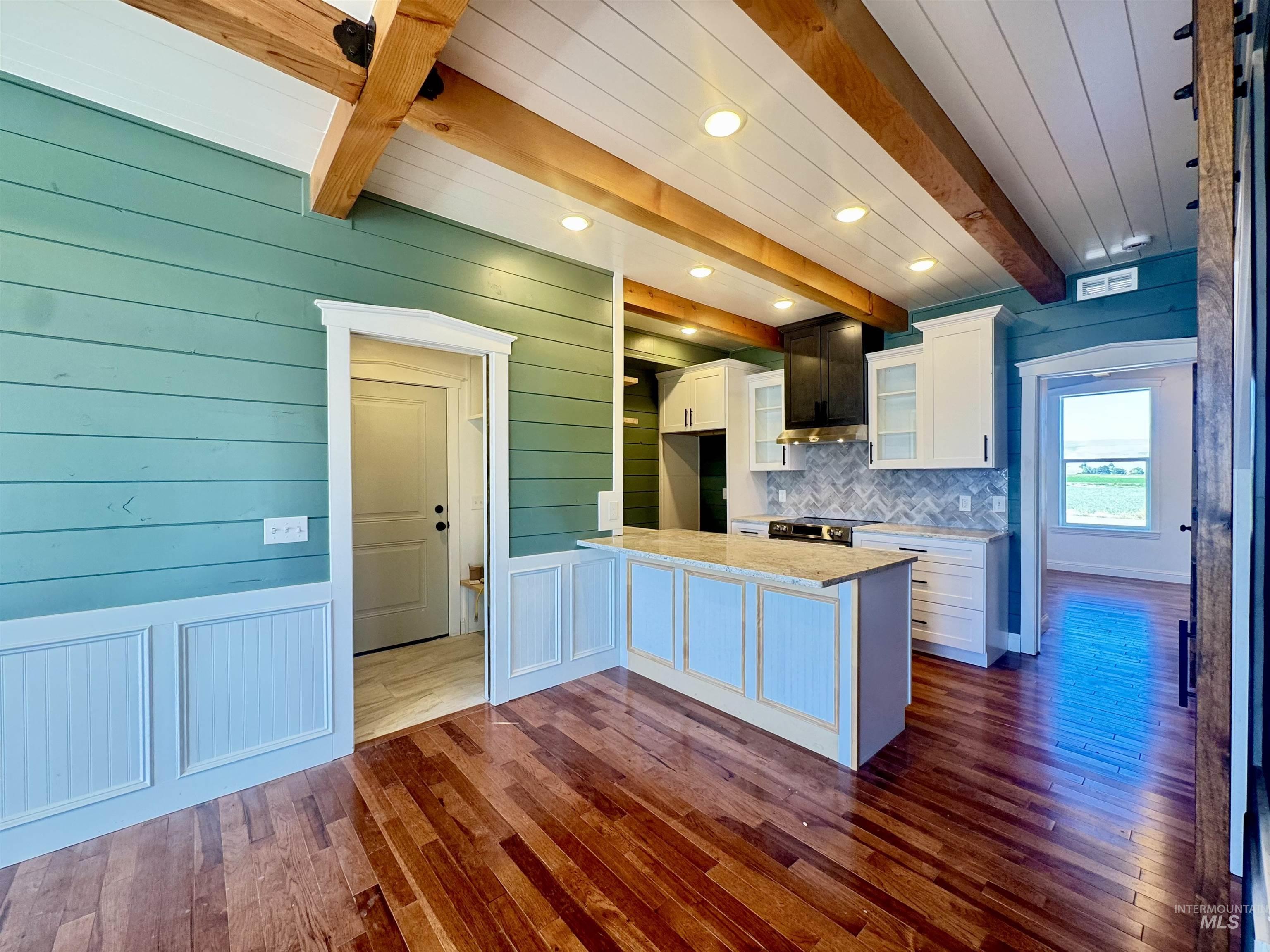 Kitchen with white cabinets, beamed ceiling, glass insert cabinets, dark wood finished floors, and a peninsula