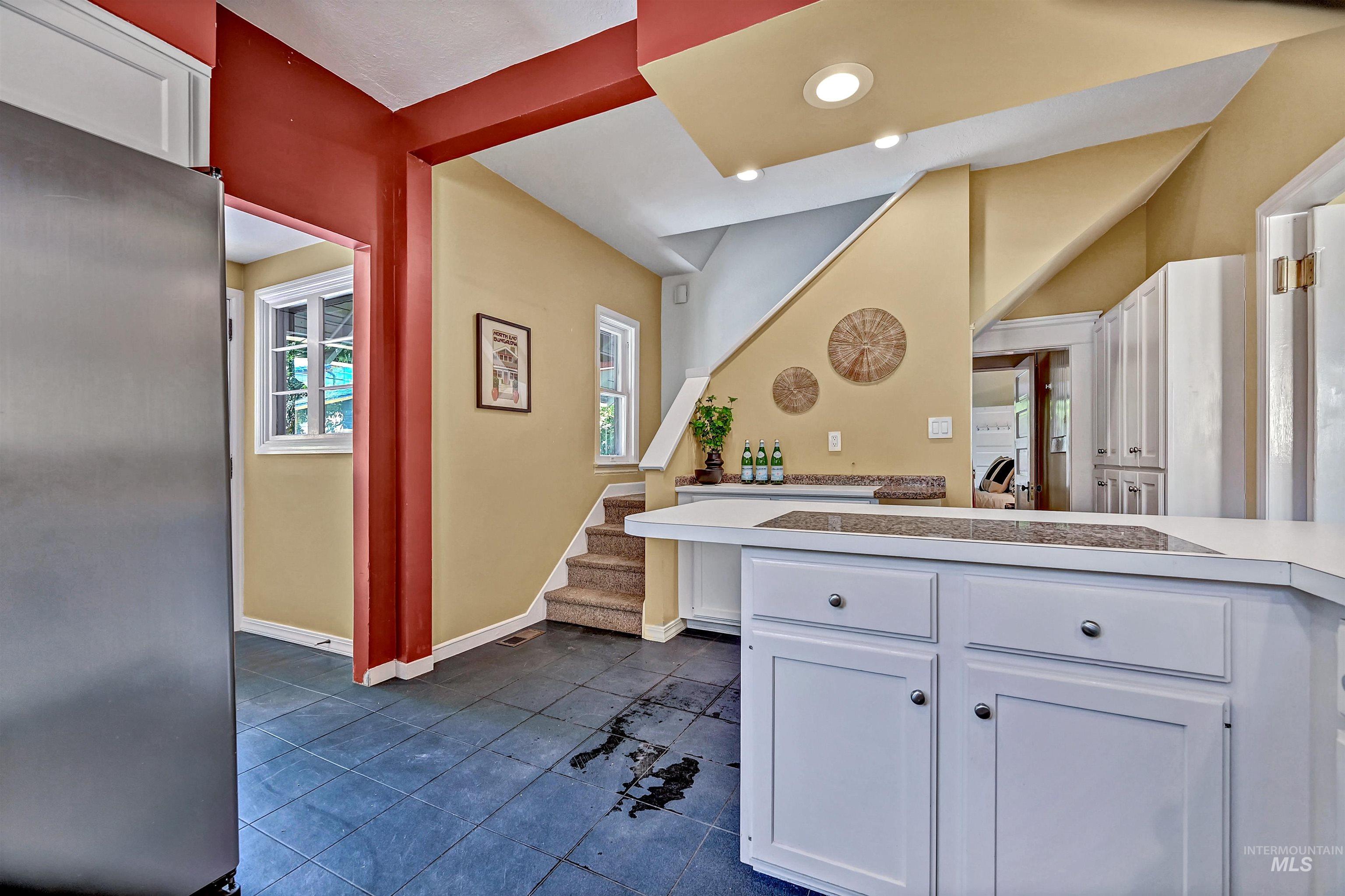 Kitchen with white cabinets, stainless steel fridge, light countertops, recessed lighting, and dark tile patterned flooring