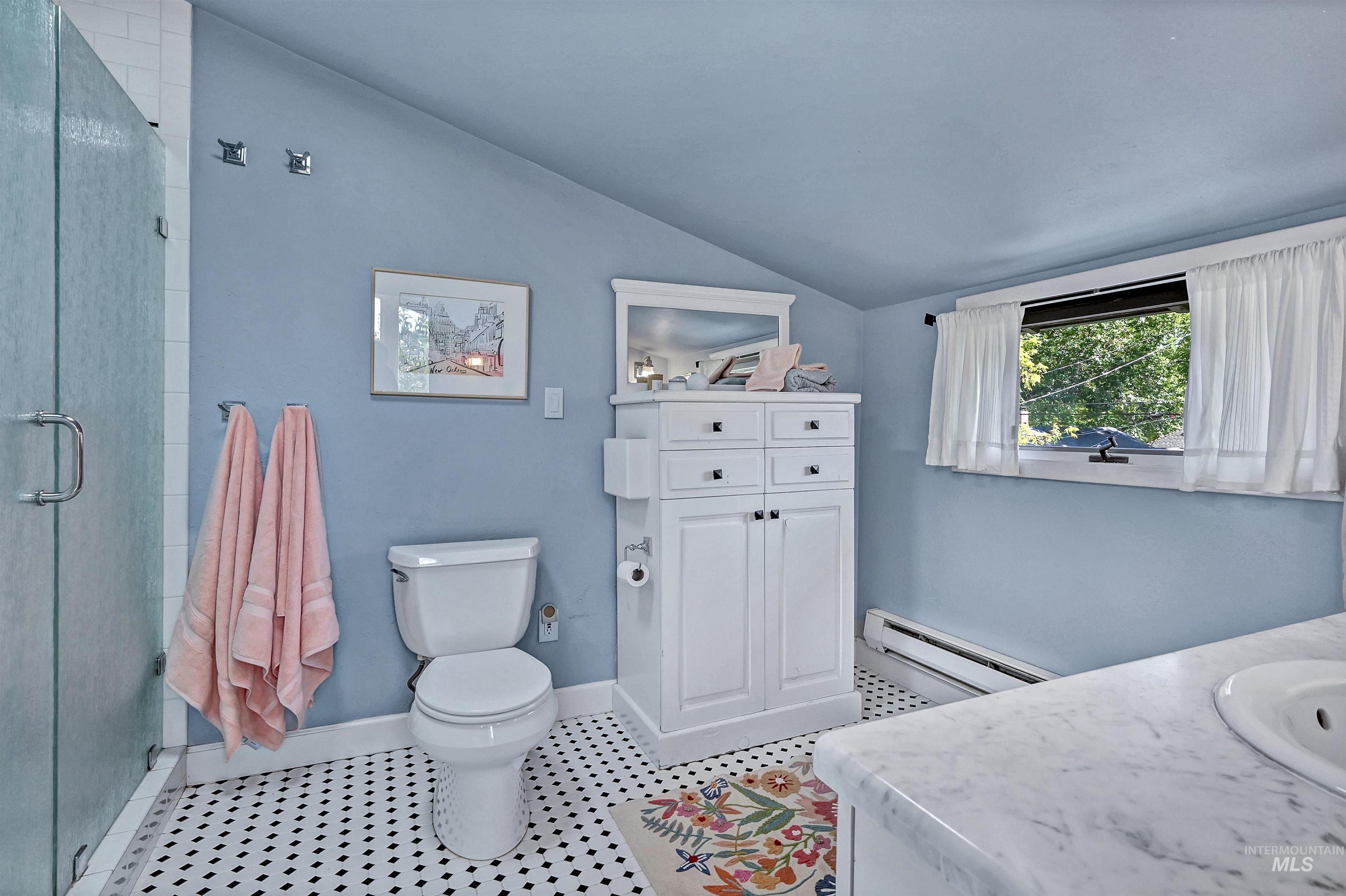 Bathroom featuring vanity, vaulted ceiling, a baseboard radiator, a walk-in shower, and light tile patterned flooring