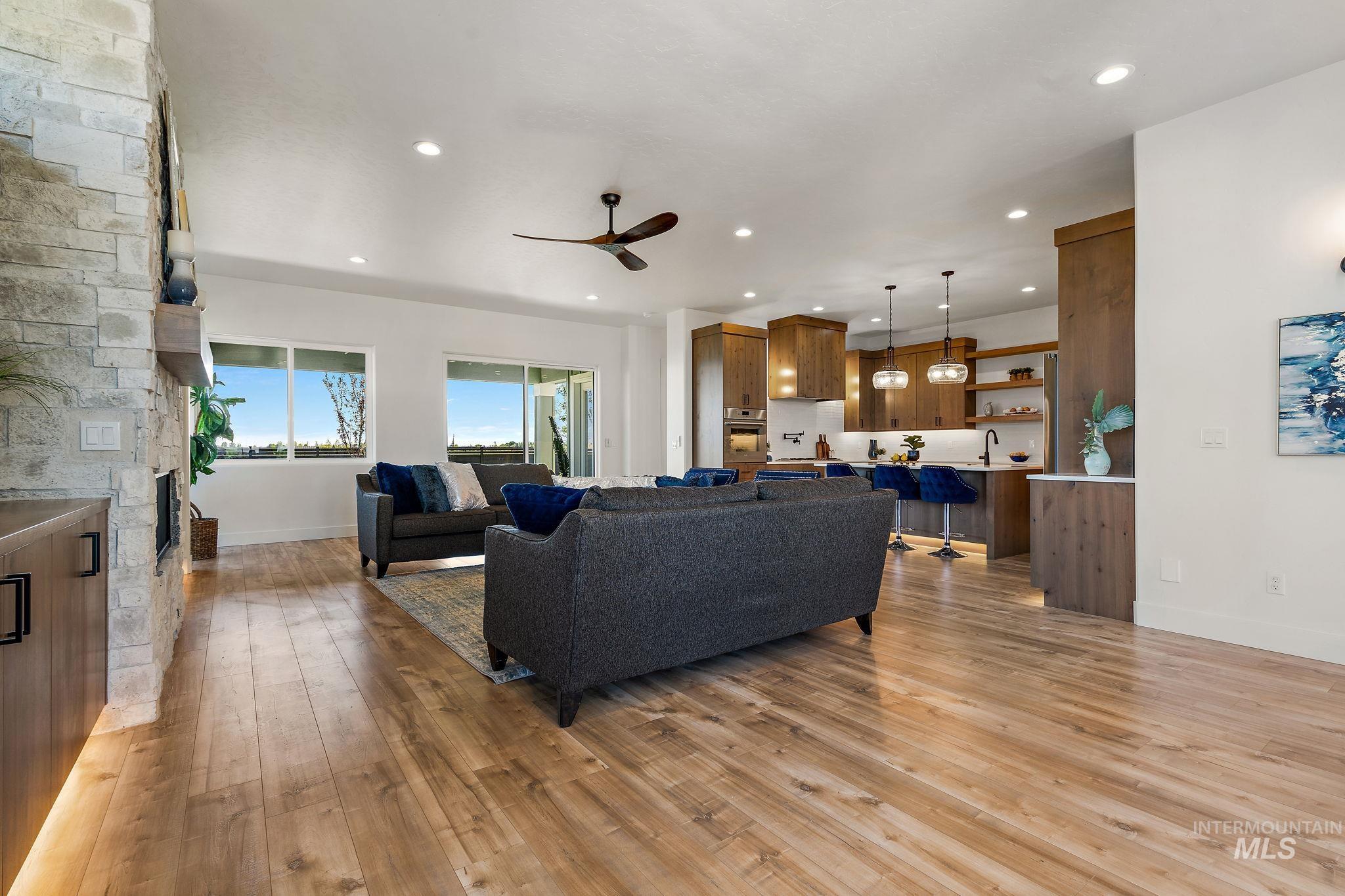 Living room featuring recessed lighting, a ceiling fan, a stone fireplace, and light wood-type flooring