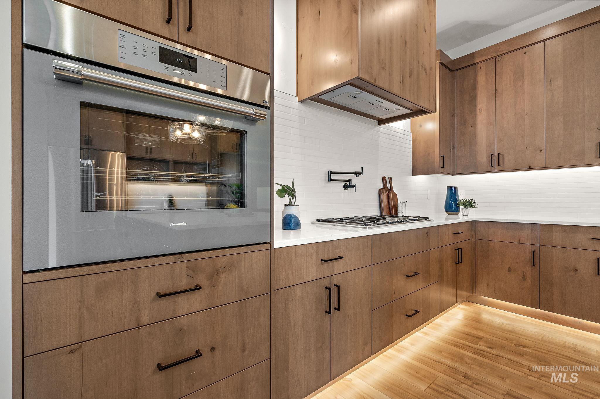 Kitchen featuring backsplash, light wood-style floors, stainless steel appliances, light stone countertops, and brown cabinets