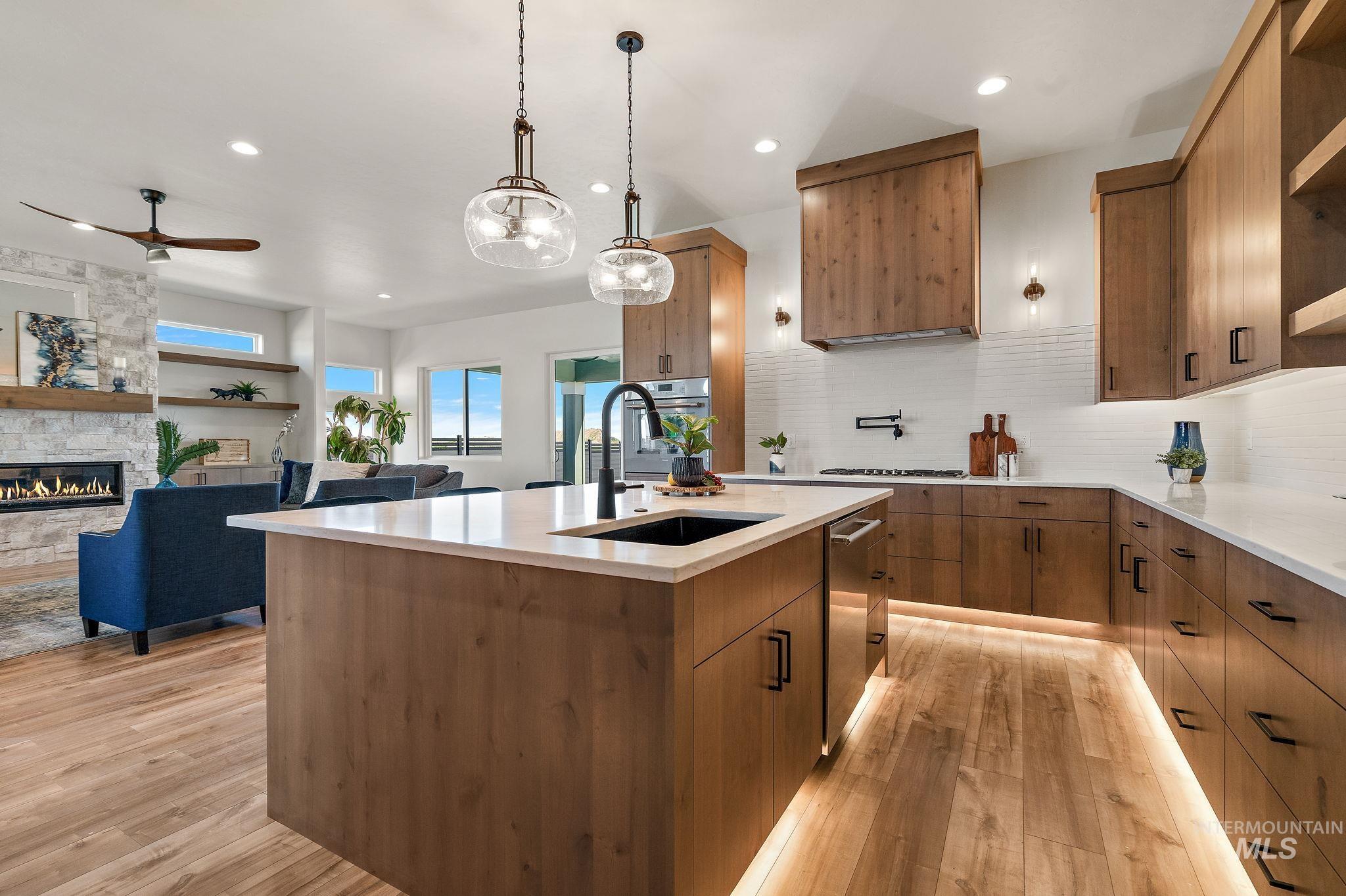 Kitchen with open floor plan, brown cabinetry, decorative light fixtures, light stone countertops, and recessed lighting