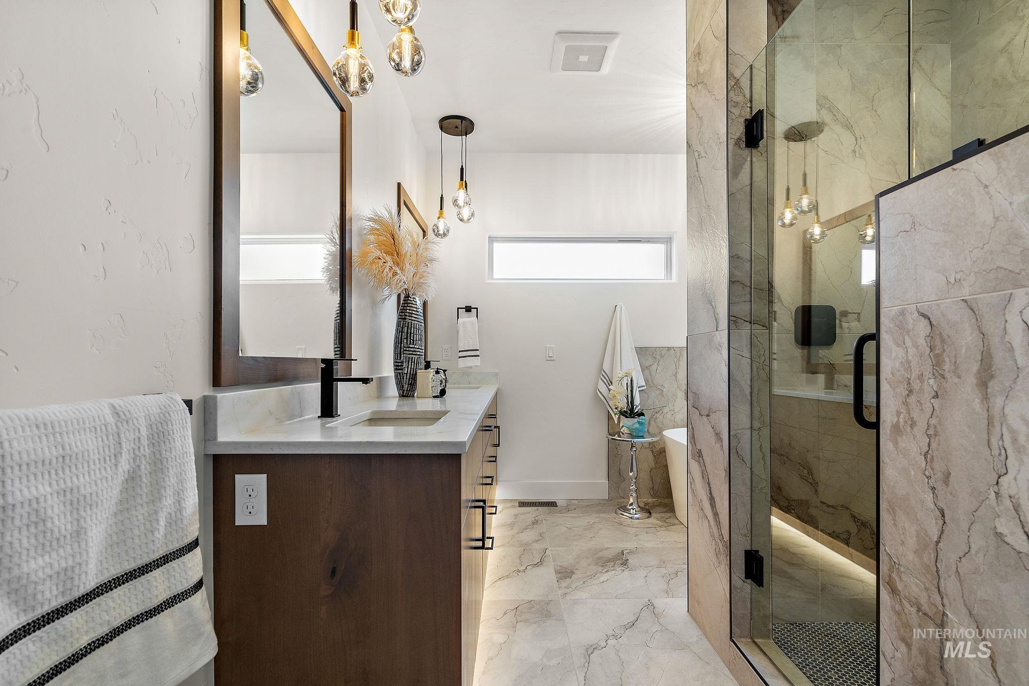 Bathroom with vanity, a freestanding tub, a marble finish shower, and light marble finish floors