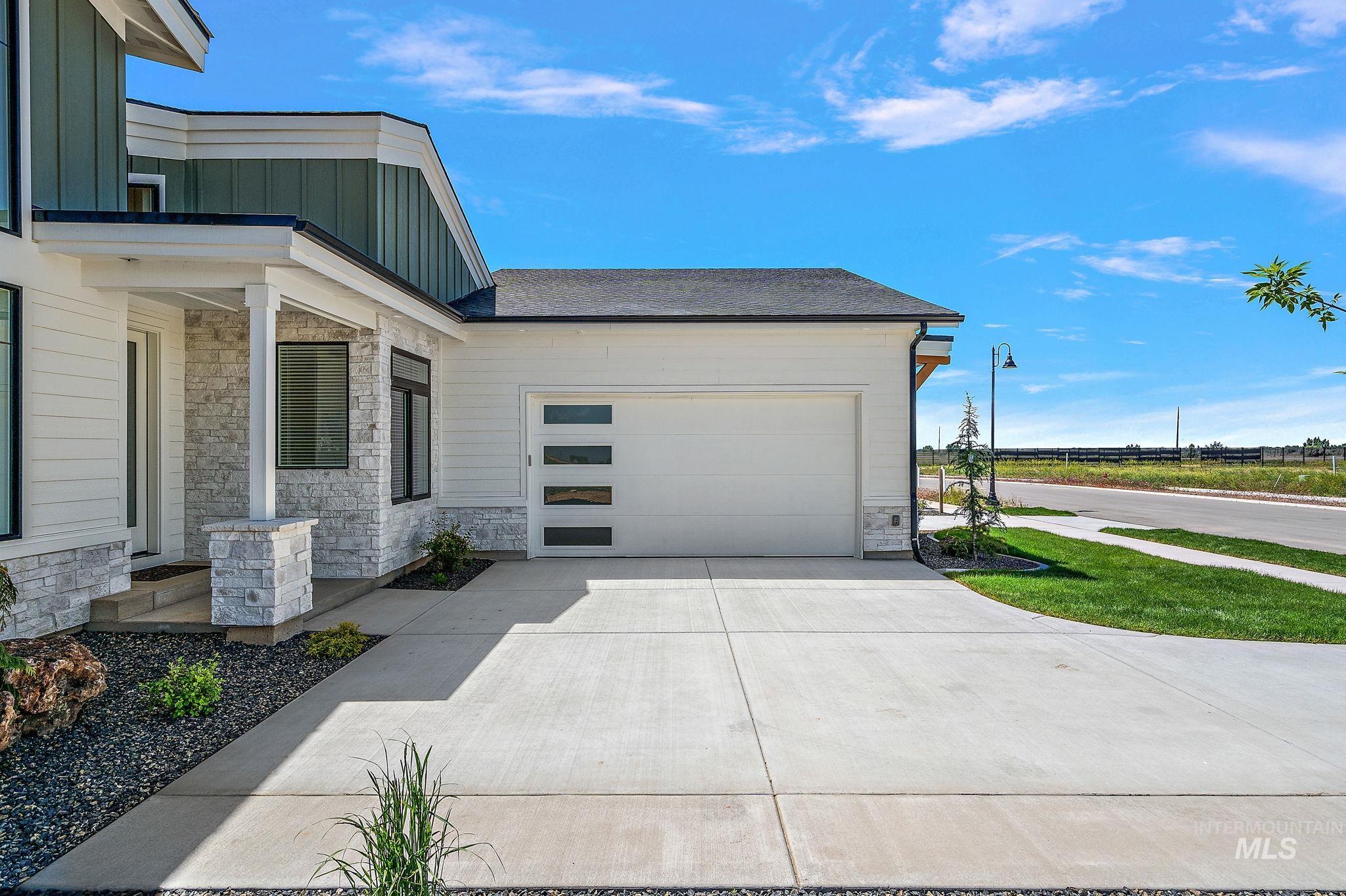 Entrance to property with stone siding, board and batten siding, concrete driveway, and an attached garage