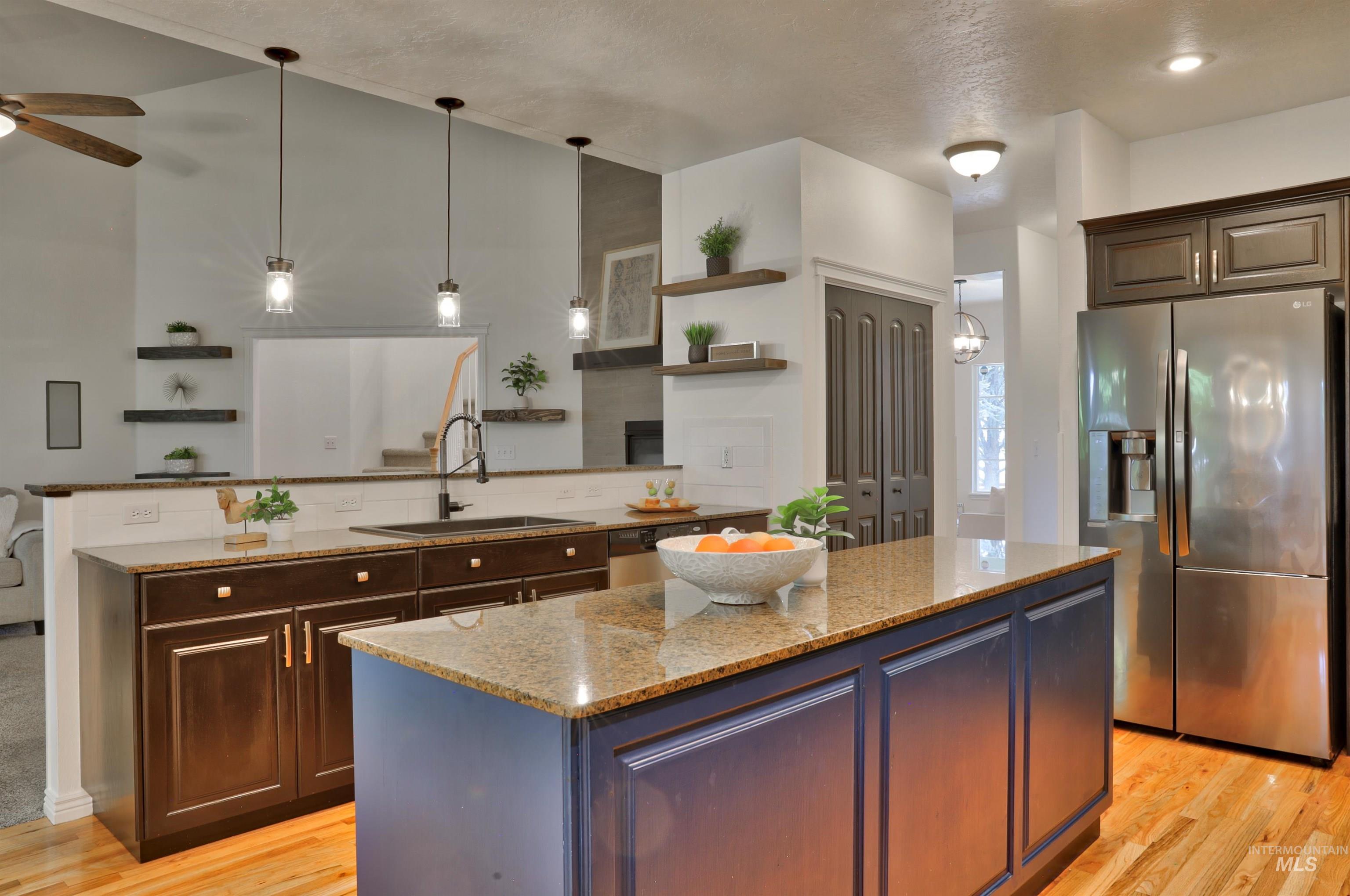 Kitchen with hanging light fixtures, appliances with stainless steel finishes, a center island, and light stone counters