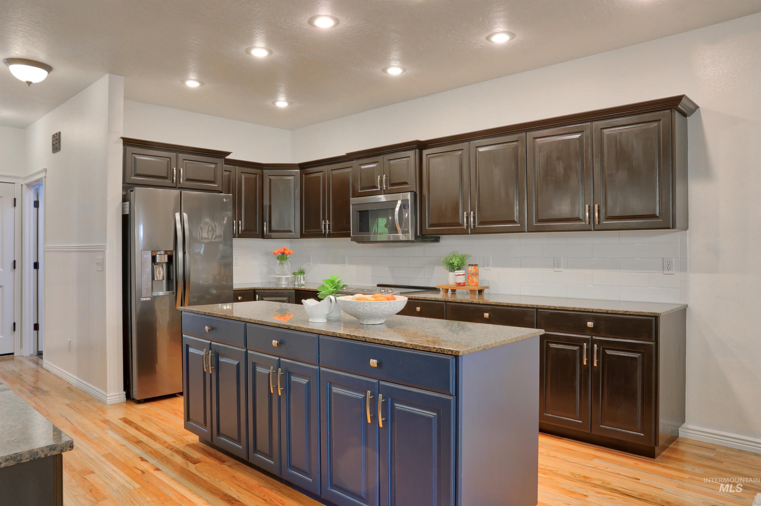 Kitchen featuring backsplash, stainless steel appliances, light wood-type flooring, light stone countertops, and dark brown cabinets