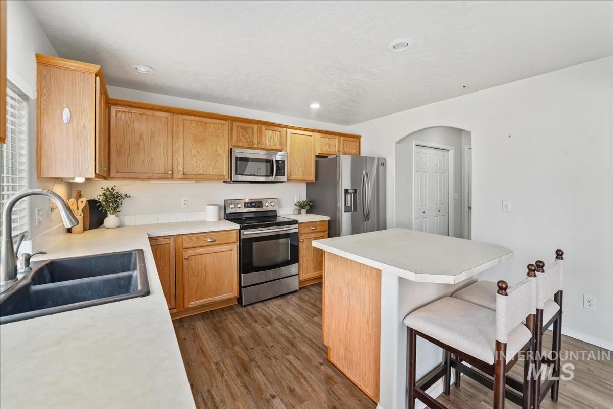 Kitchen with stainless steel appliances, light countertops, a breakfast bar, dark wood-style floors, and arched walkways