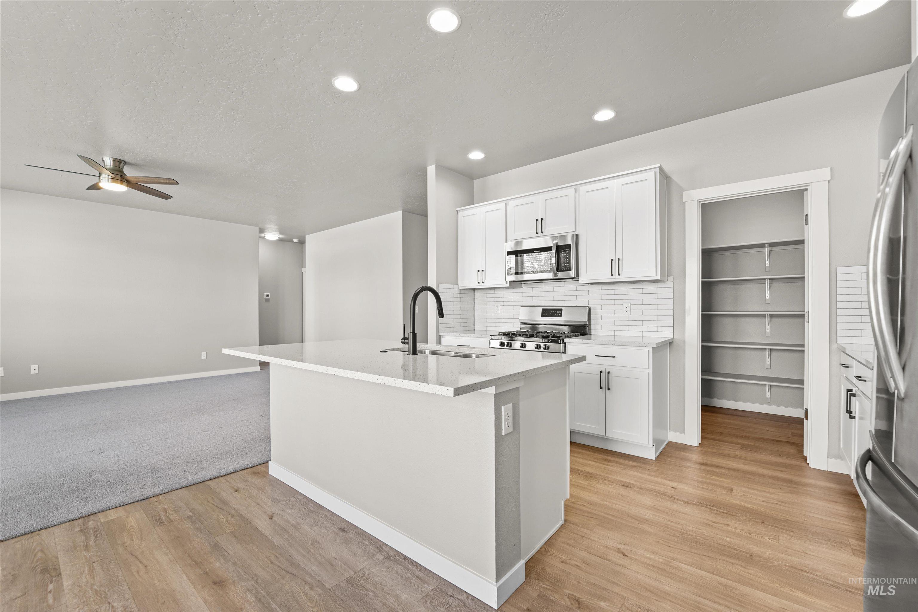 Kitchen featuring decorative backsplash, white cabinets, a center island with sink, stainless steel appliances, and open floor plan