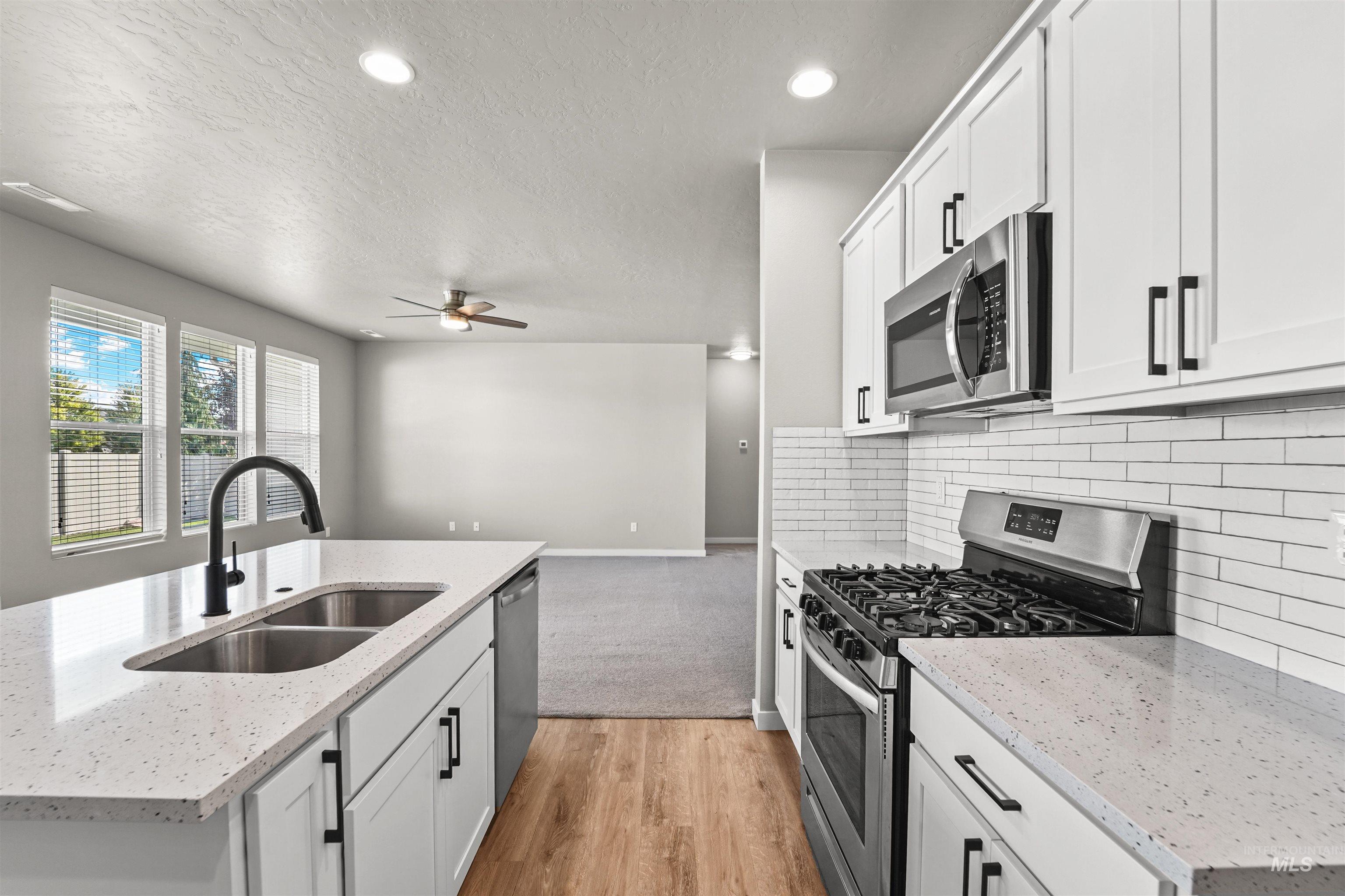 Kitchen with appliances with stainless steel finishes, light stone counters, white cabinetry, backsplash, and a textured ceiling