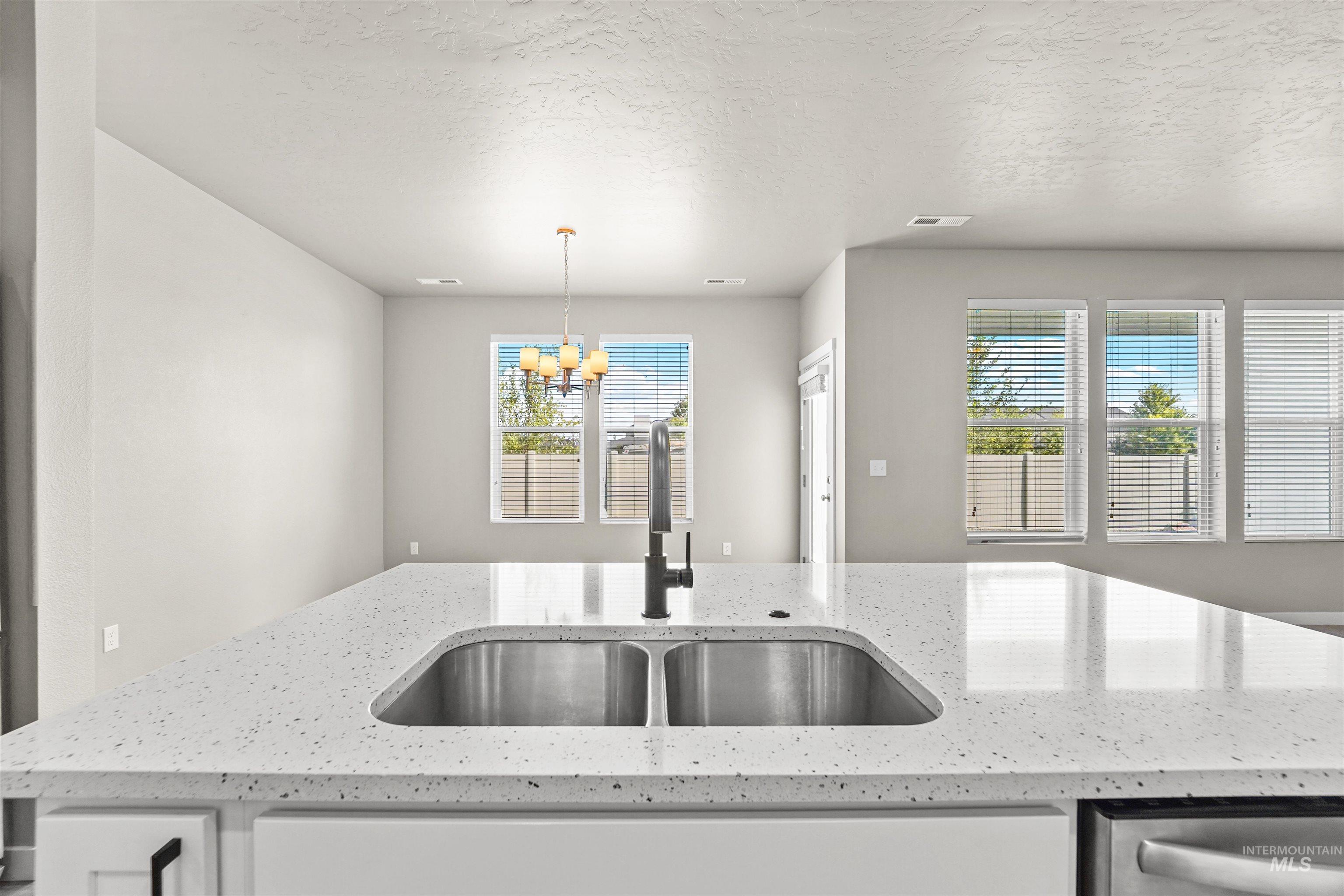 Kitchen with light stone countertops, a textured ceiling, a chandelier, and decorative light fixtures