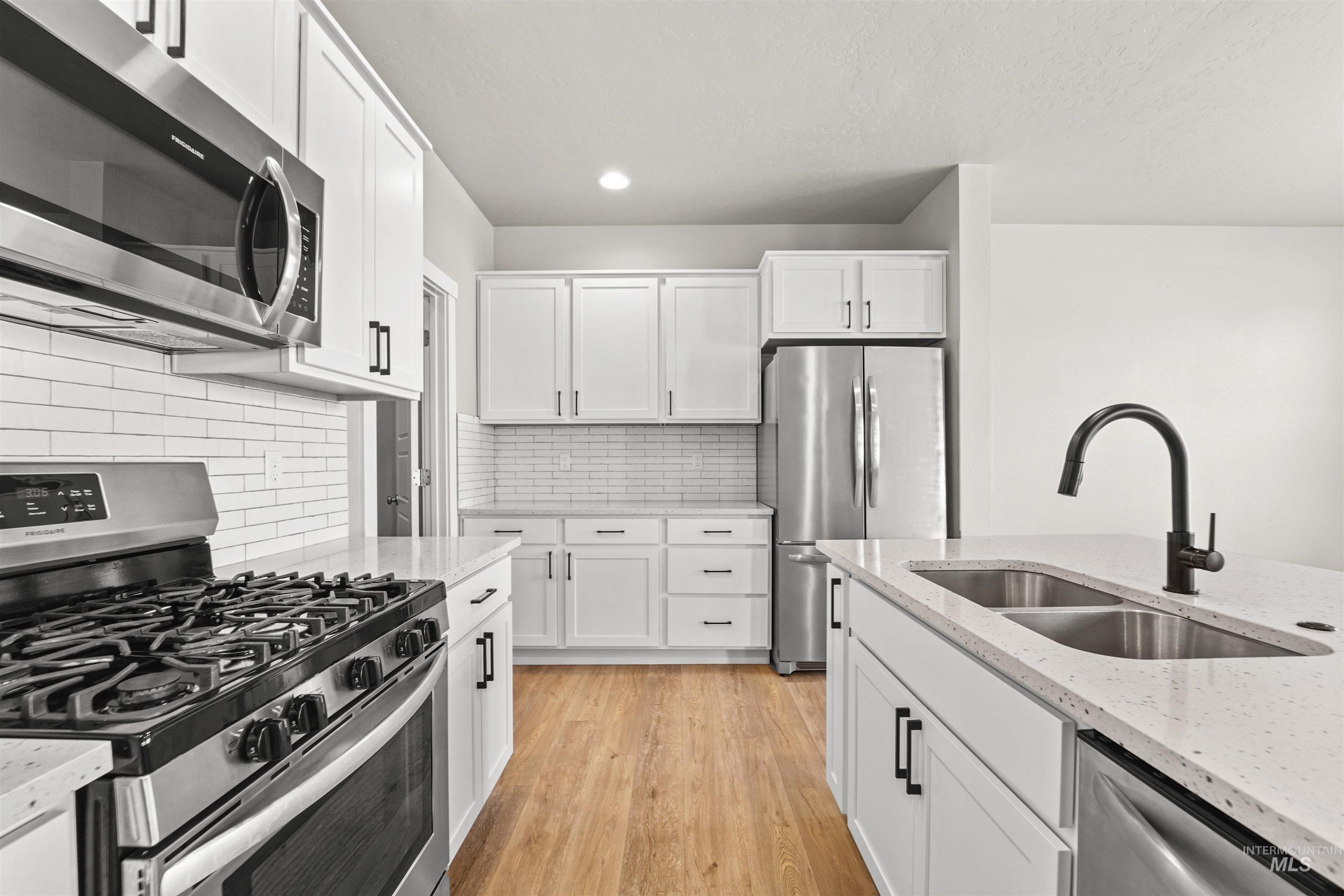 Kitchen with appliances with stainless steel finishes, backsplash, white cabinets, light wood-style flooring, and light stone counters