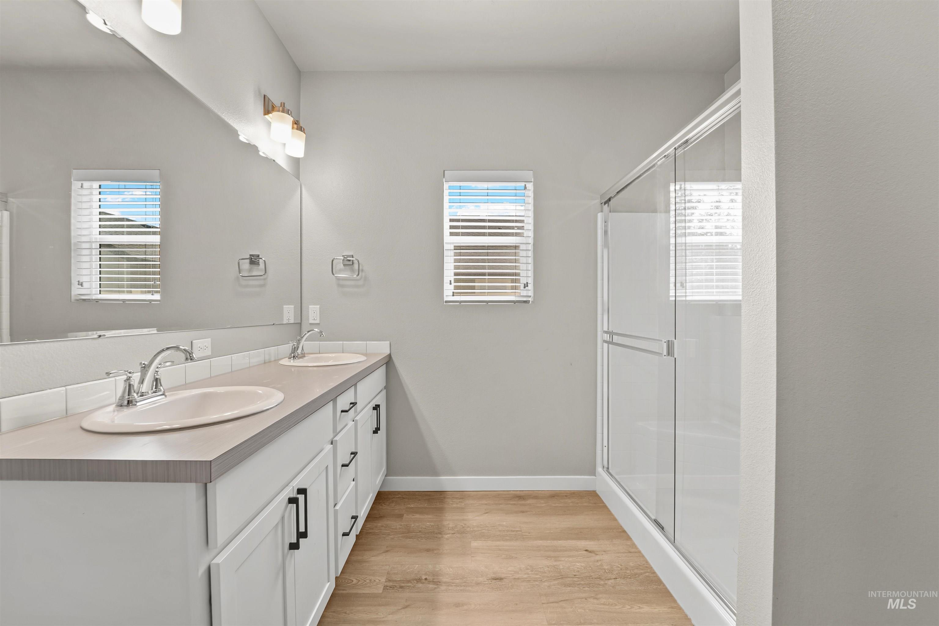 Full bath featuring double vanity, a stall shower, and light wood-style floors