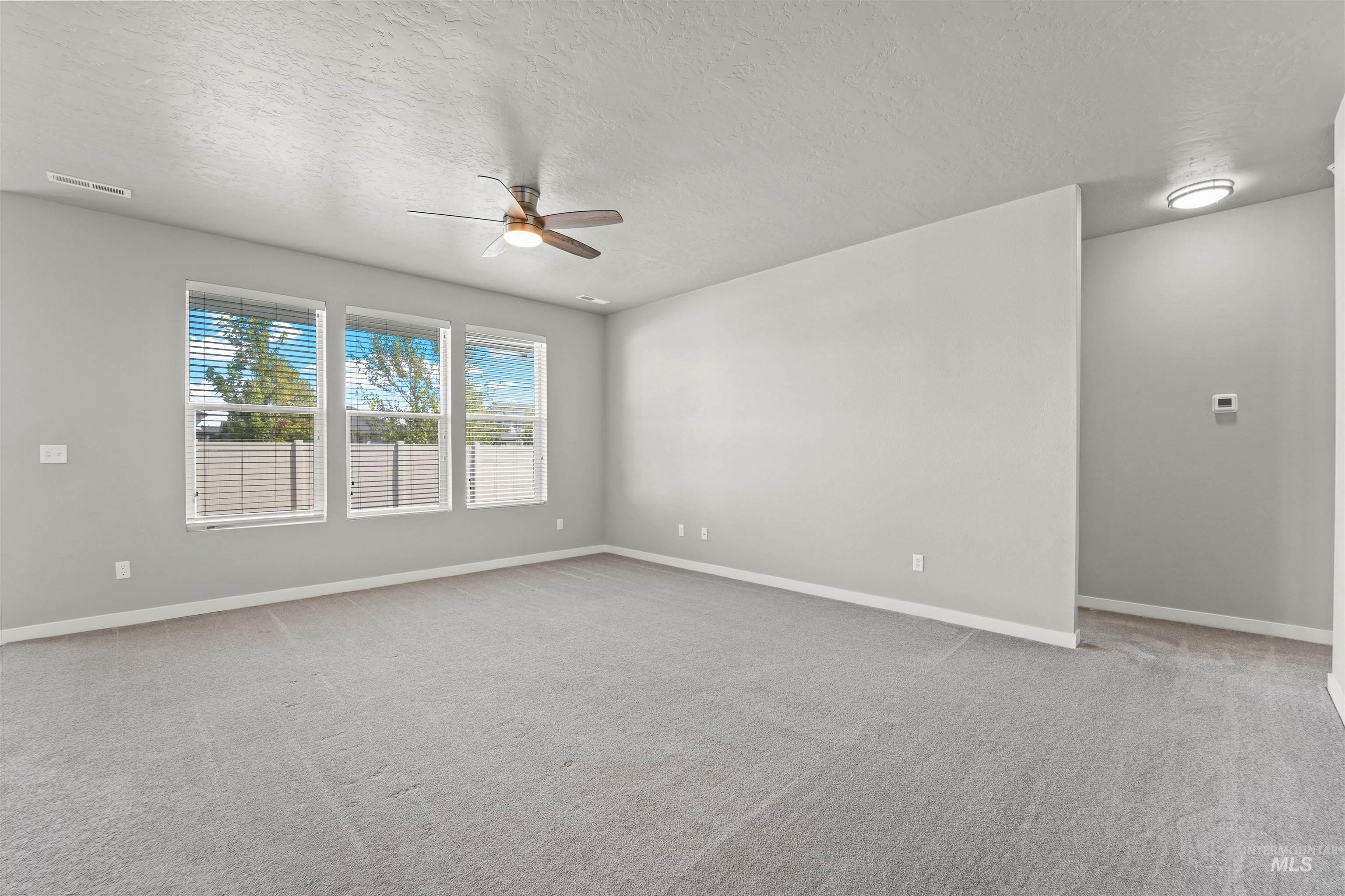 Empty room featuring light colored carpet, a textured ceiling, and ceiling fan