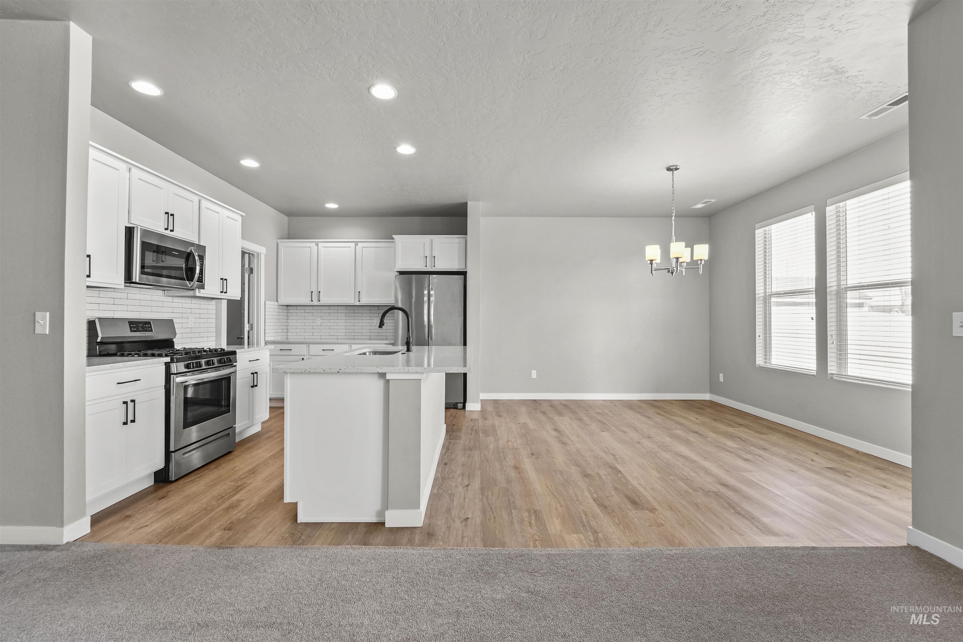 Kitchen with appliances with stainless steel finishes, white cabinetry, tasteful backsplash, a center island with sink, and recessed lighting