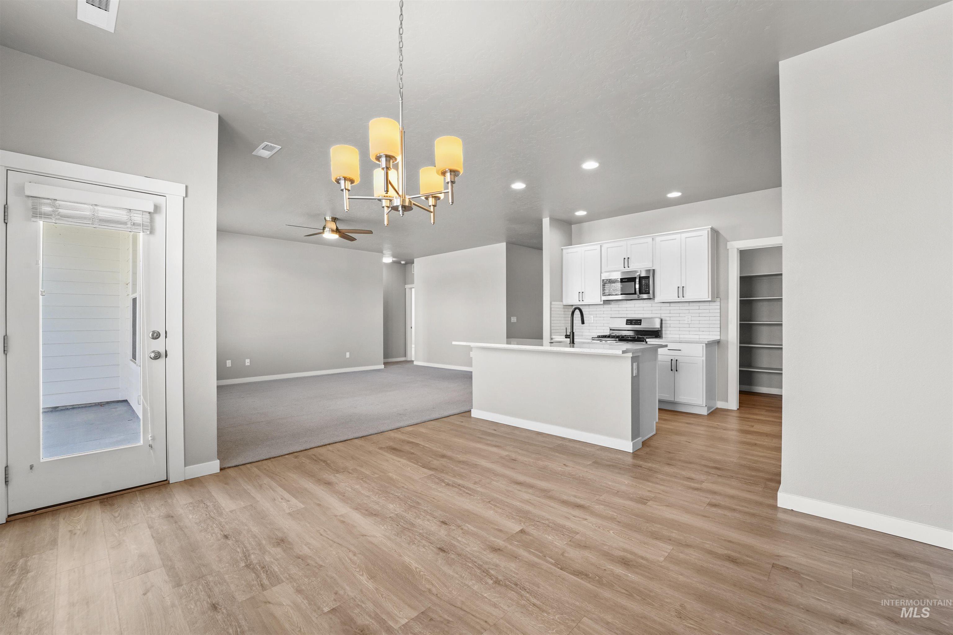 Kitchen featuring pendant lighting, open floor plan, a chandelier, white cabinets, and backsplash