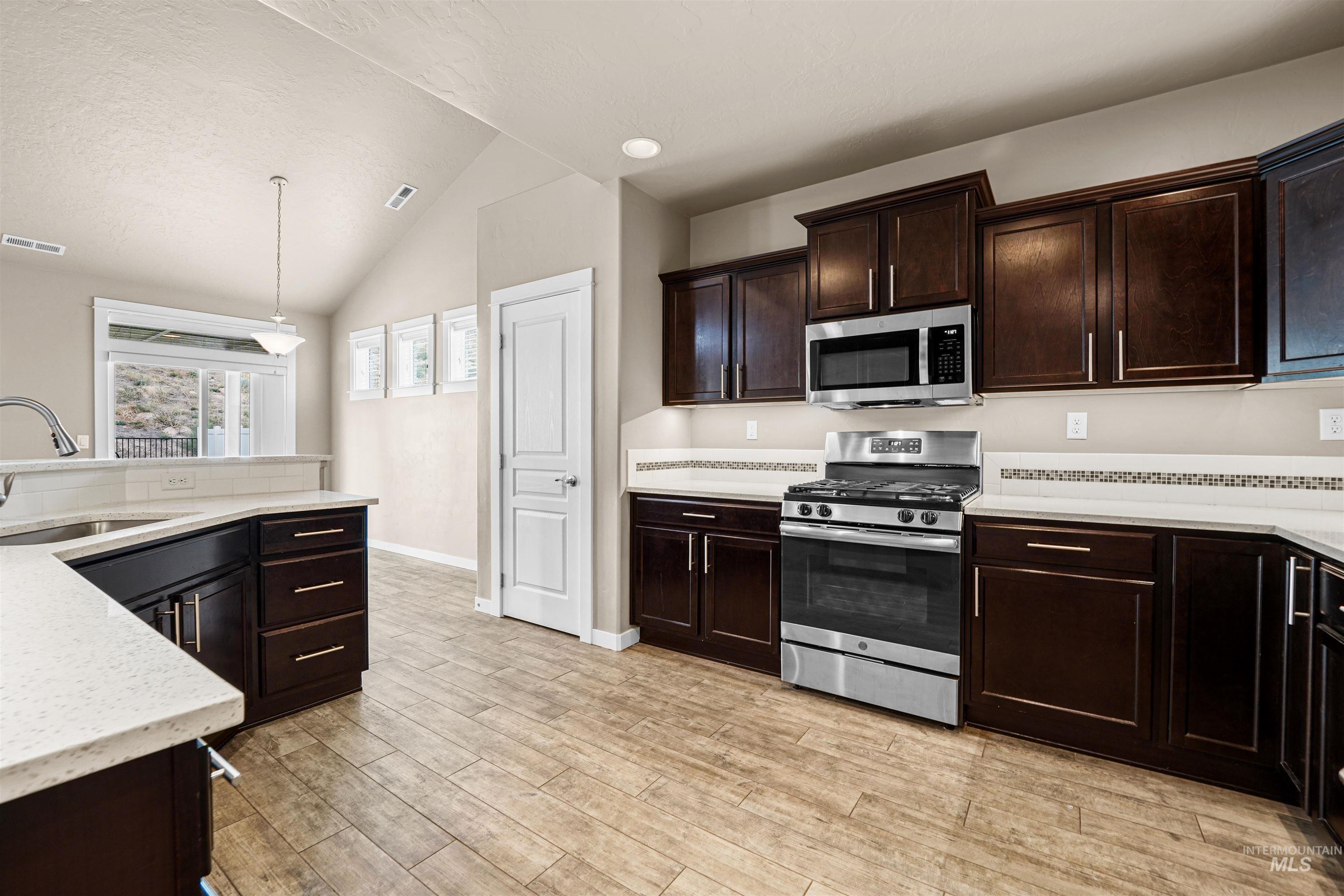 Kitchen featuring appliances with stainless steel finishes, lofted ceiling, decorative light fixtures, dark brown cabinetry, and a textured ceiling