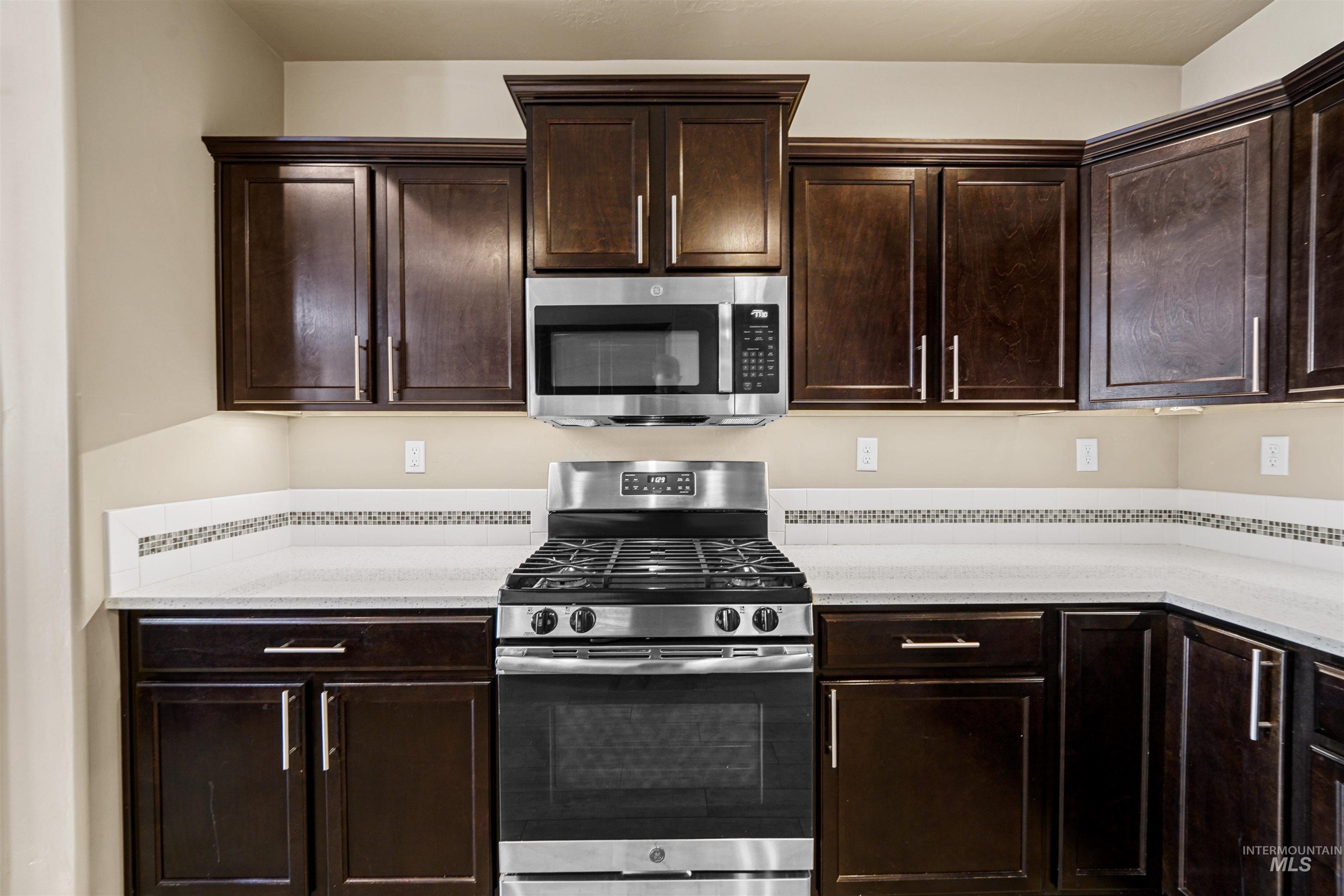 Kitchen featuring stainless steel appliances, dark brown cabinetry, and light stone countertops
