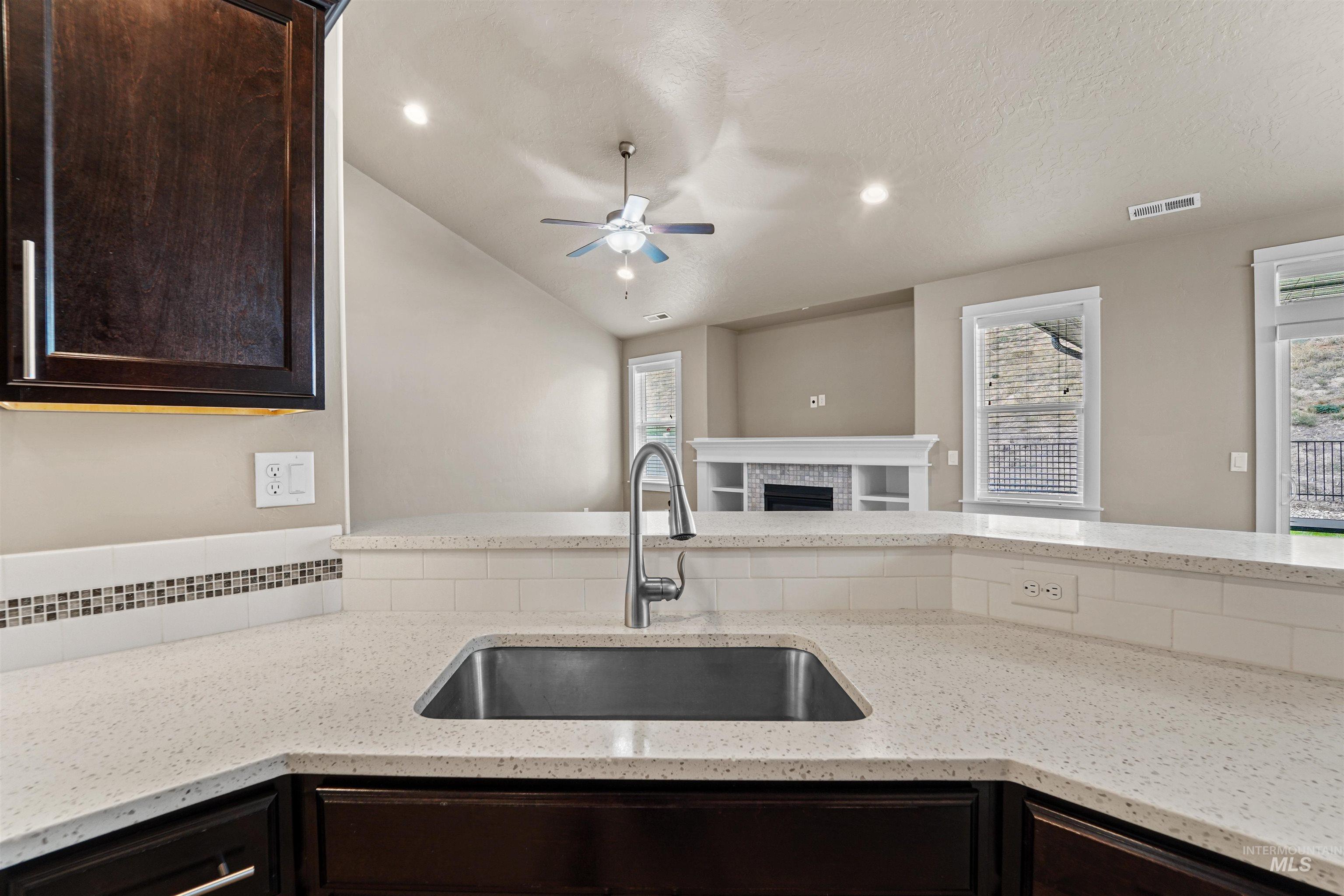 Kitchen with light stone countertops, dark brown cabinetry, a fireplace, lofted ceiling, and open floor plan