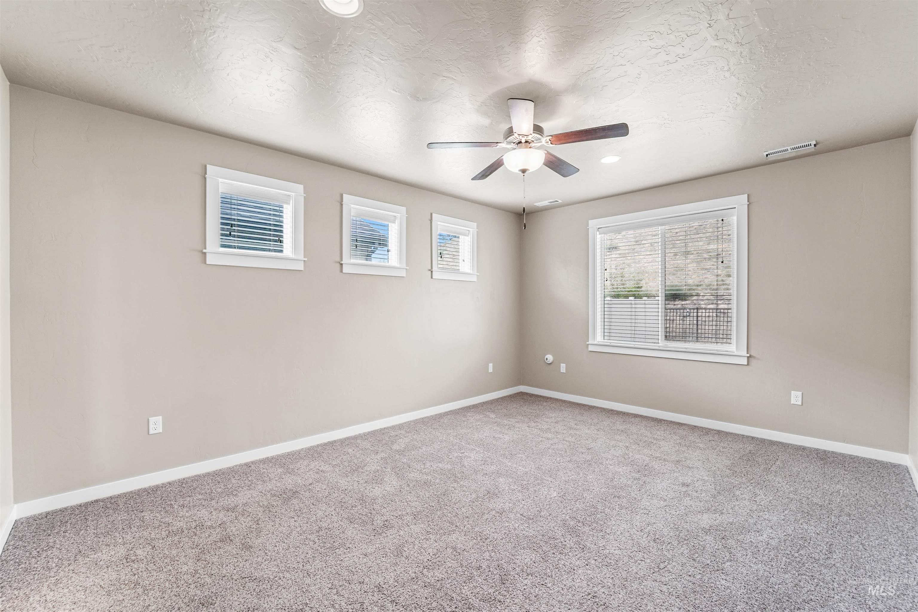 Empty room featuring light colored carpet, a textured ceiling, and ceiling fan