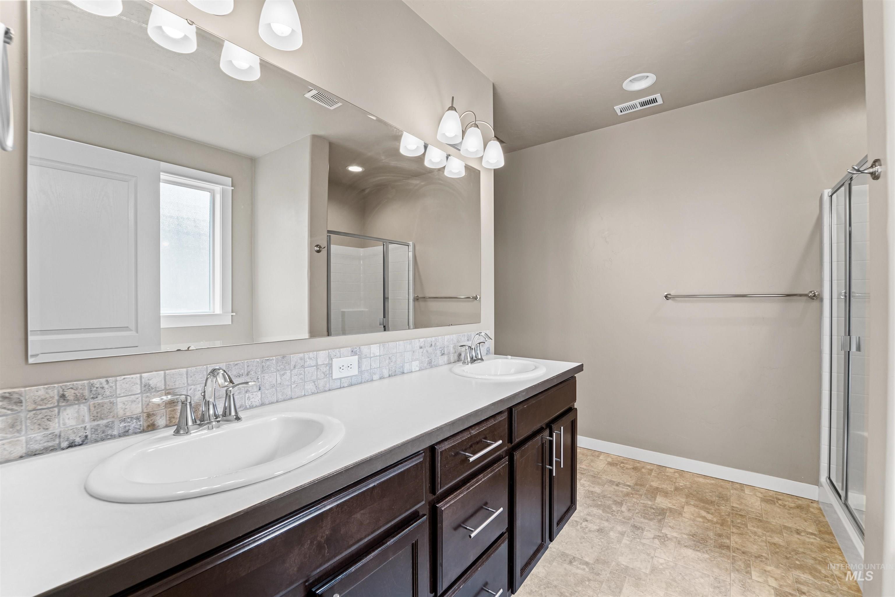 Bathroom featuring a stall shower, double vanity, and decorative backsplash