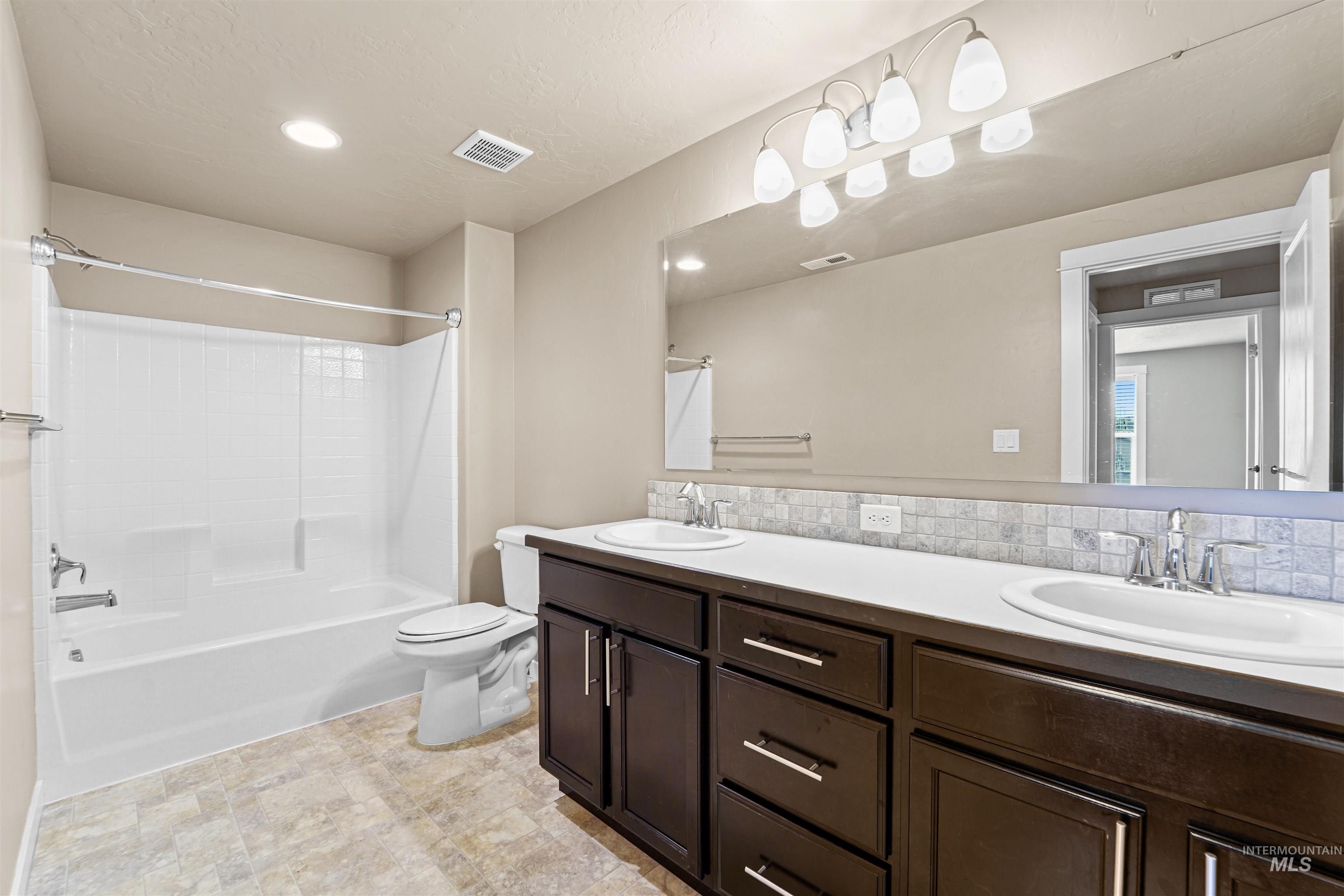Full bath featuring washtub / shower combination, double vanity, decorative backsplash, recessed lighting, and a textured ceiling